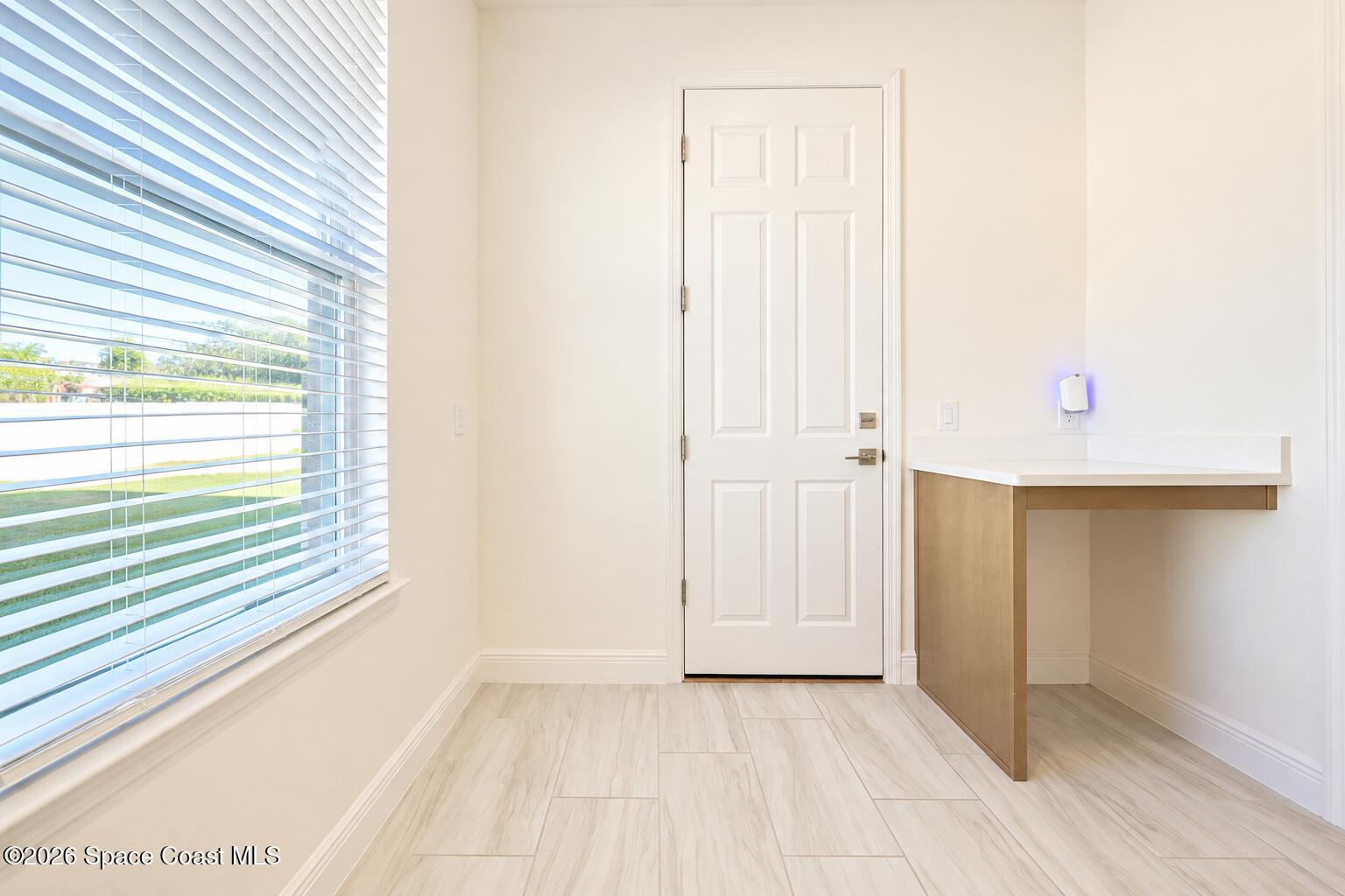 Bright entry with a white paneled door, window blinds, built-in counter, and light tile floor.
