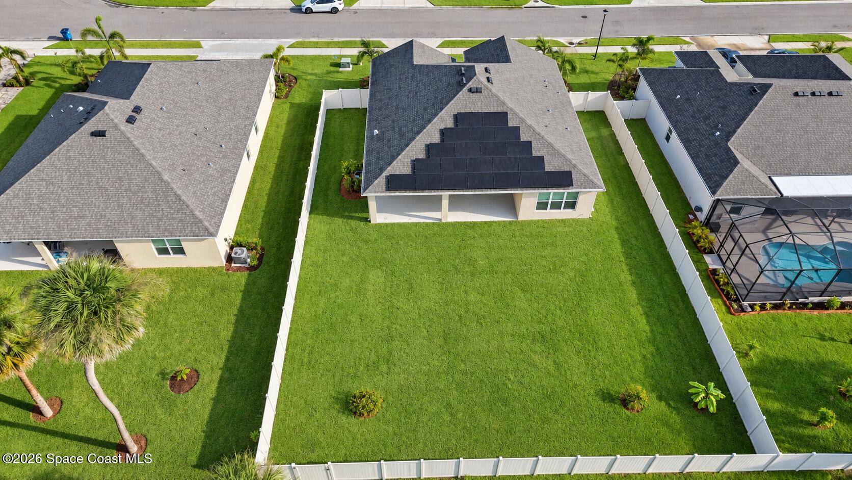 Aerial view of a home with rooftop solar panels and a large fenced lawn.
