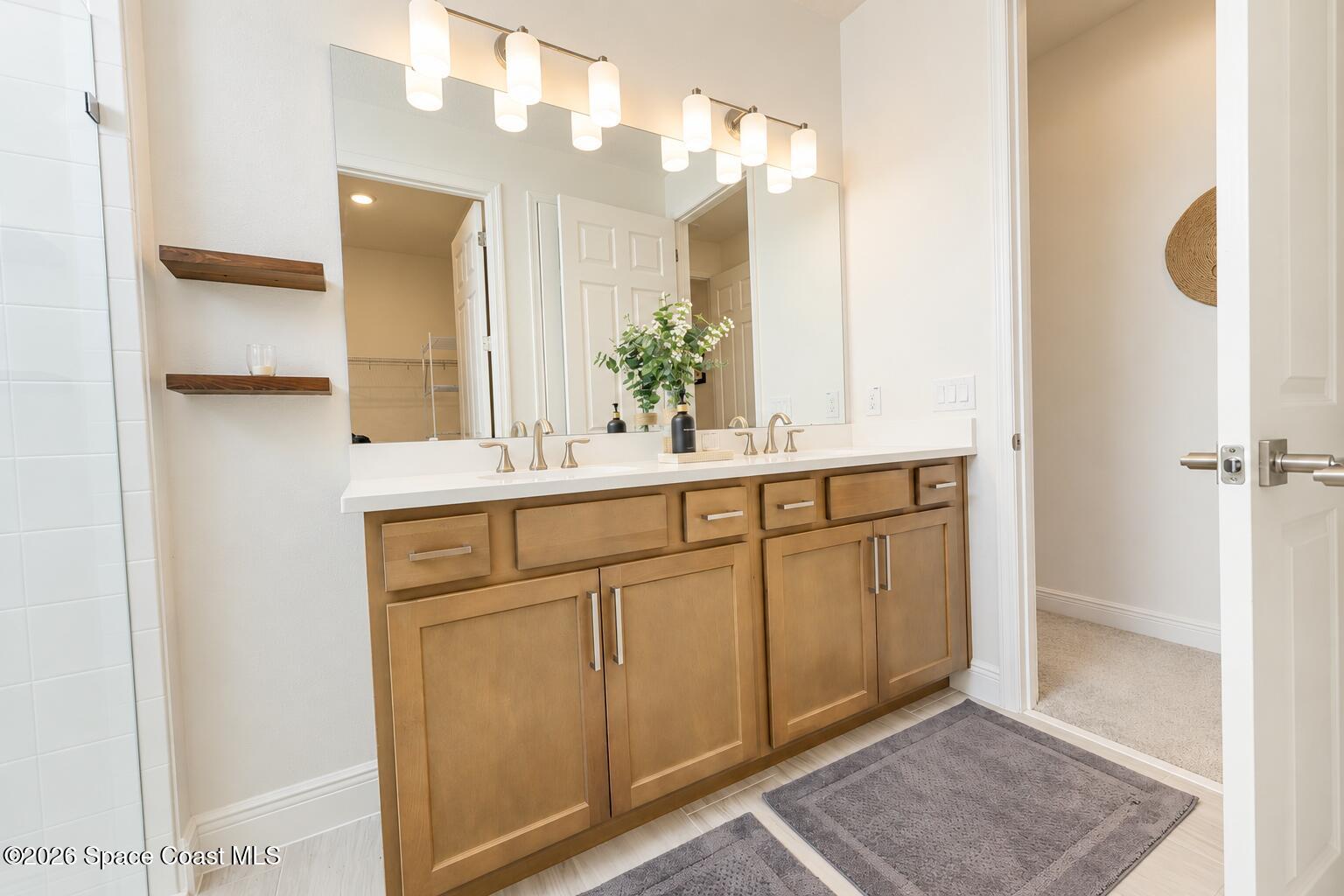 Bathroom with a double vanity, warm wood cabinetry, large mirror, and modern lights.