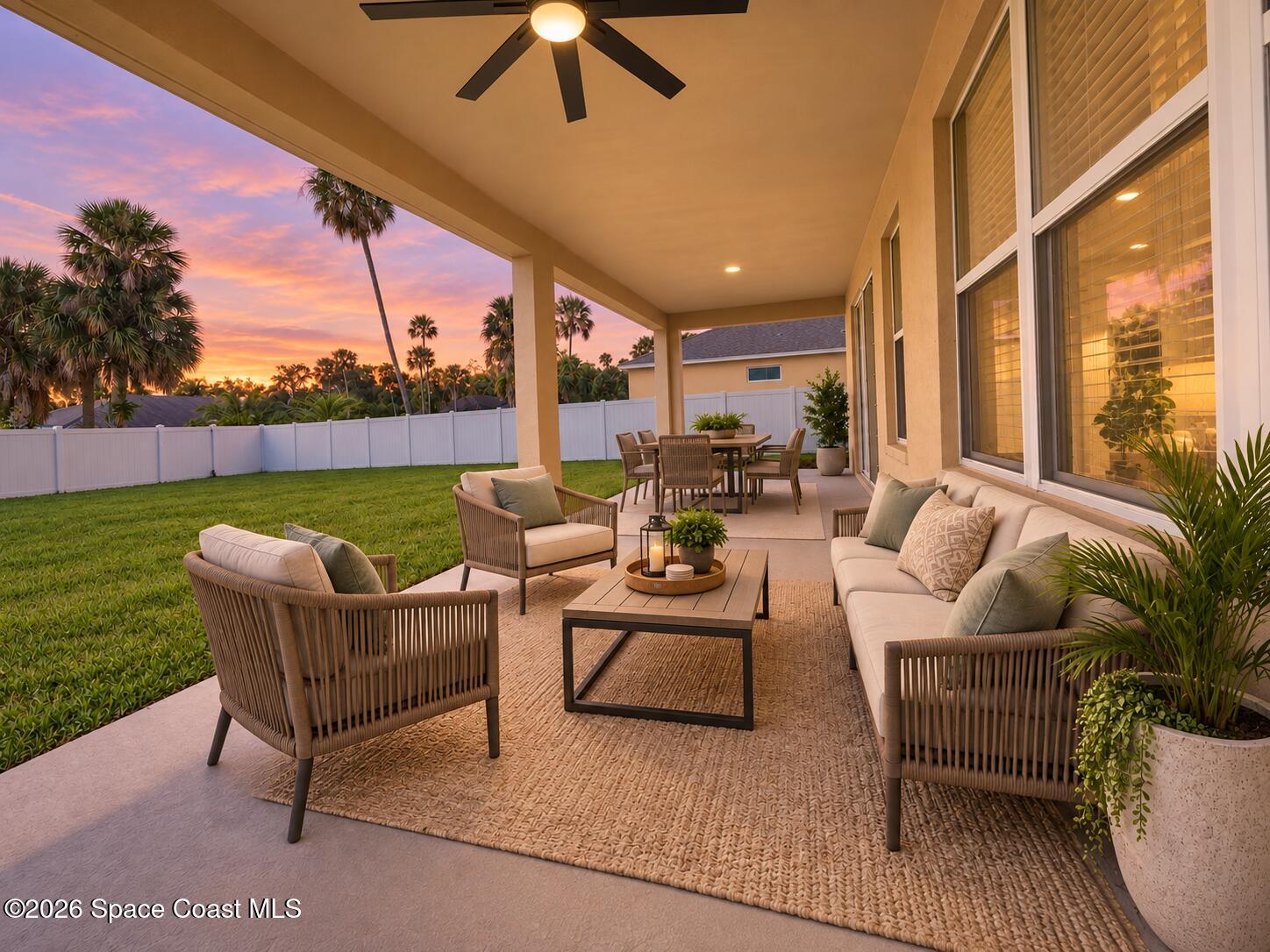 Furnished covered patio with dining and lounge seating overlooking a fenced lawn at sunset.
