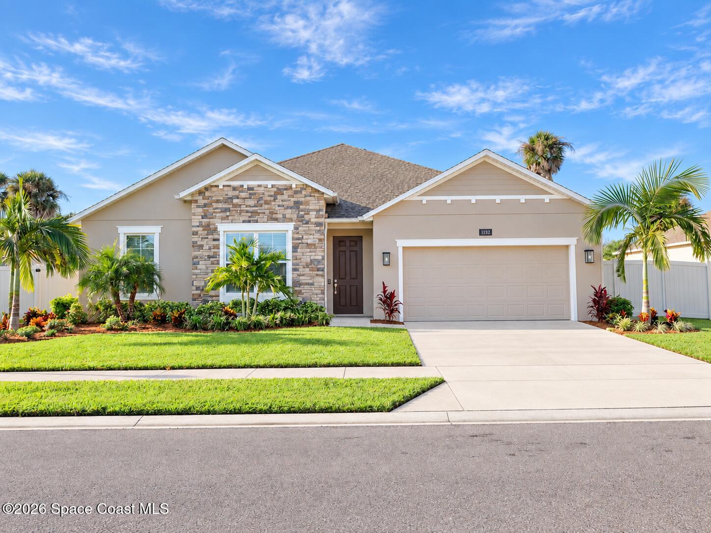 Single-story home with stone facade, two-car garage, palms, and landscaped front lawn.