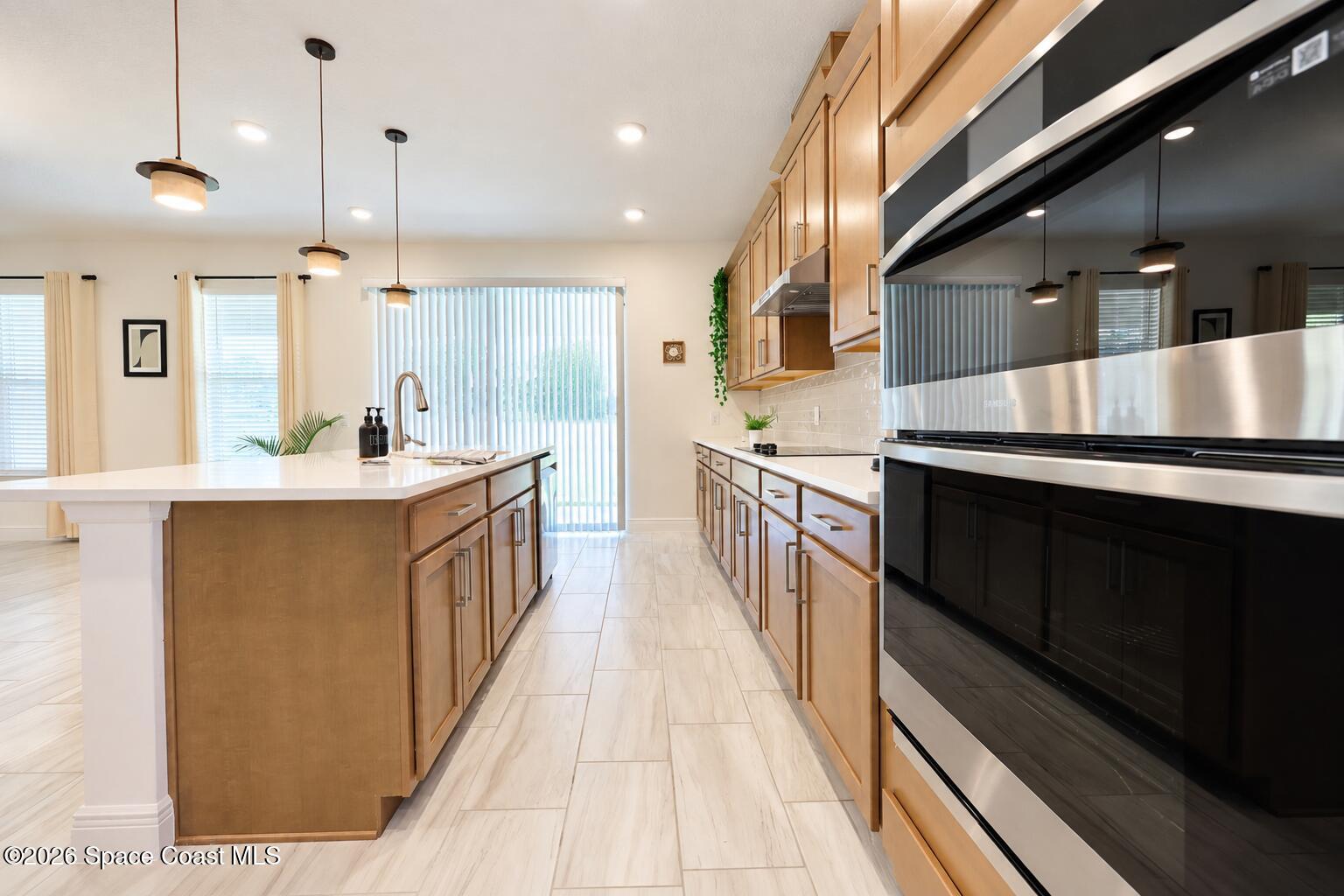 Kitchen with a large white island, warm wood cabinetry, and stainless steel appliances.