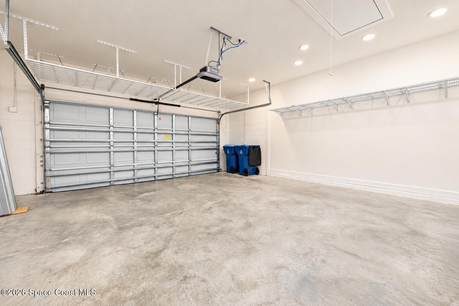 Empty garage with a closed sectional door and overhead storage racks.