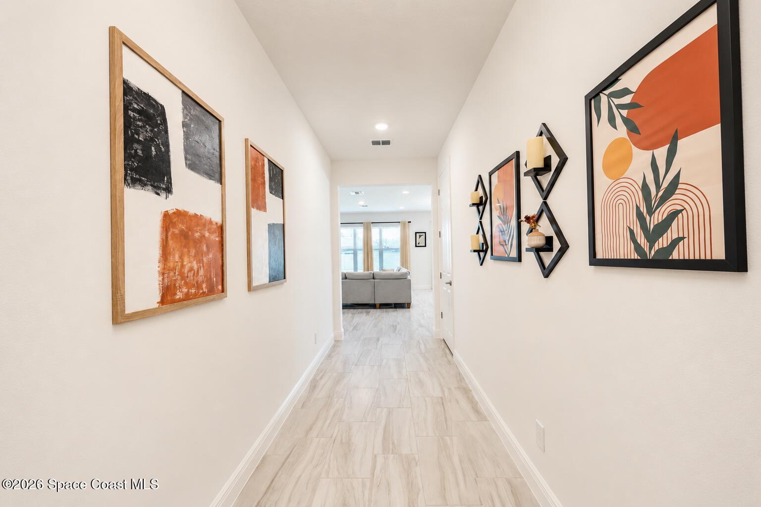 Bright hallway with light tile floors and framed artwork leading to a living room.