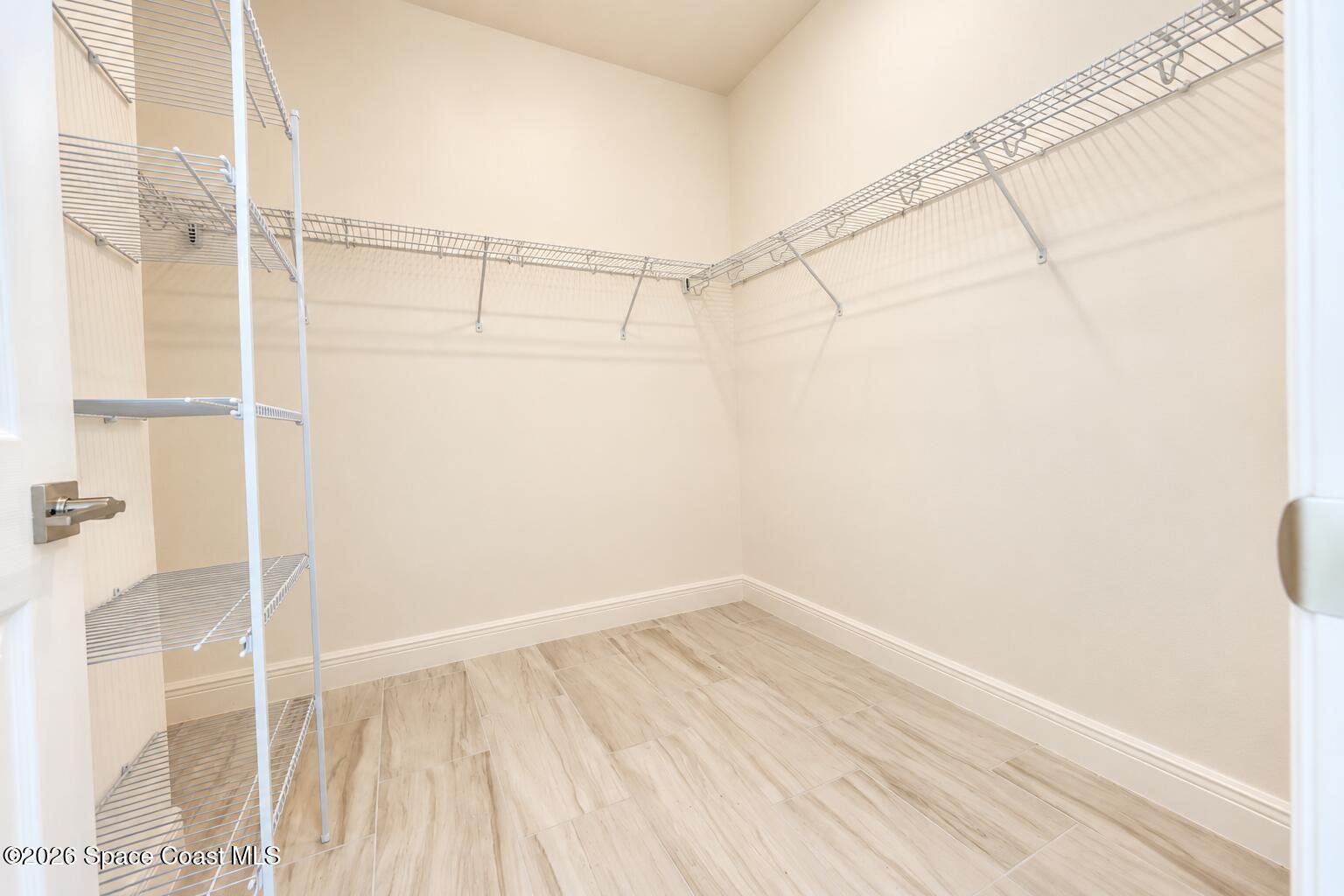 Walk-in closet with white wire shelving and light wood-look tile flooring.