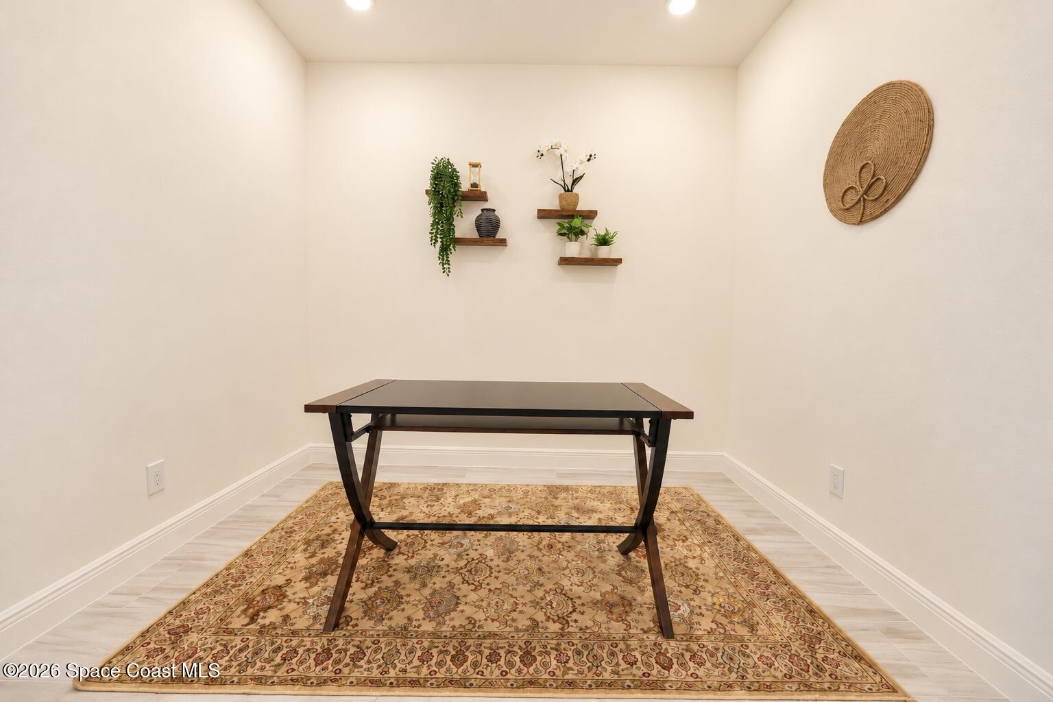 Small staged office with a dark wood desk, patterned rug, and plant-filled floating shelves.
