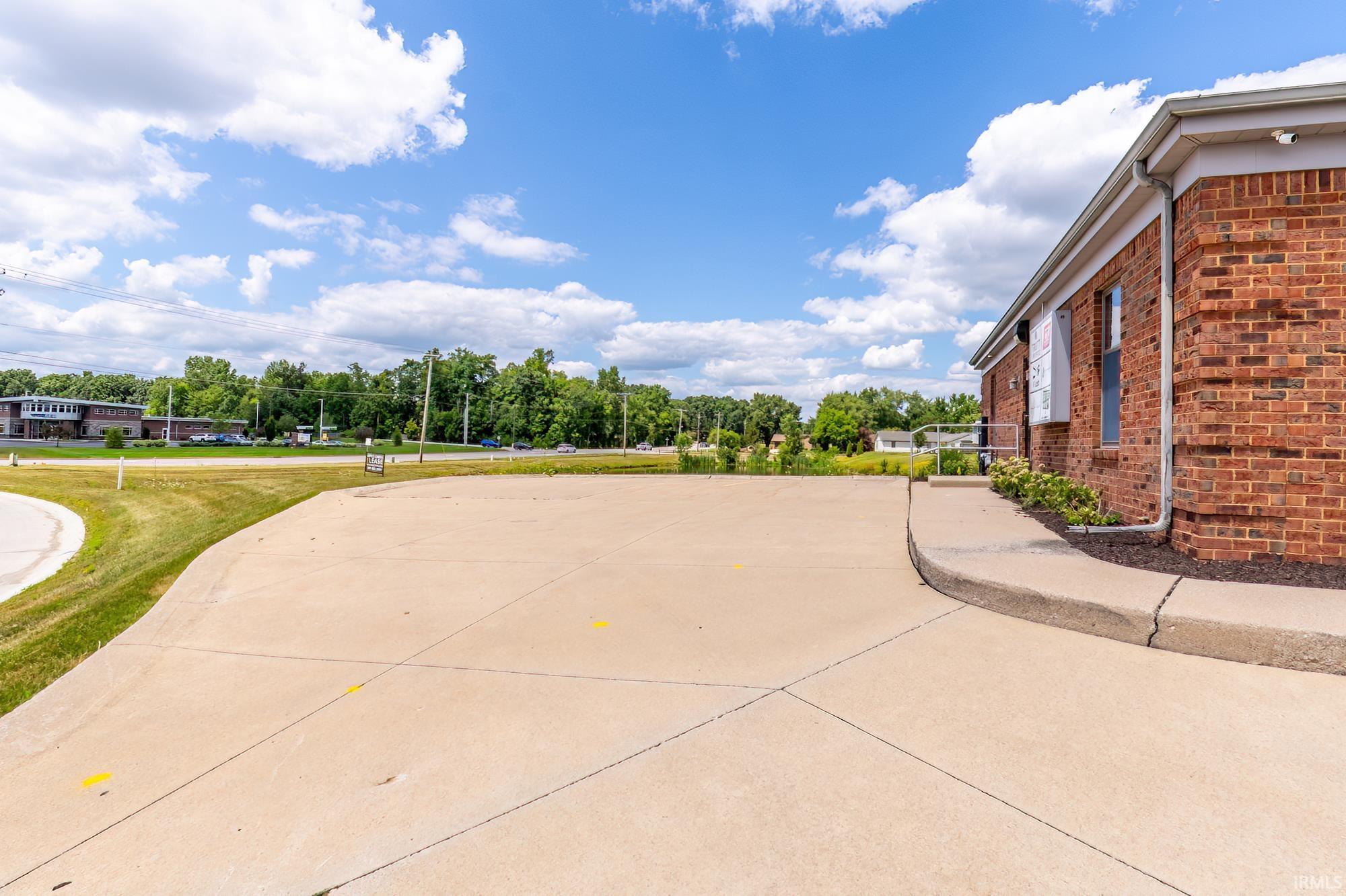 Red brick commercial building beside a broad concrete paved area and raised walkway.