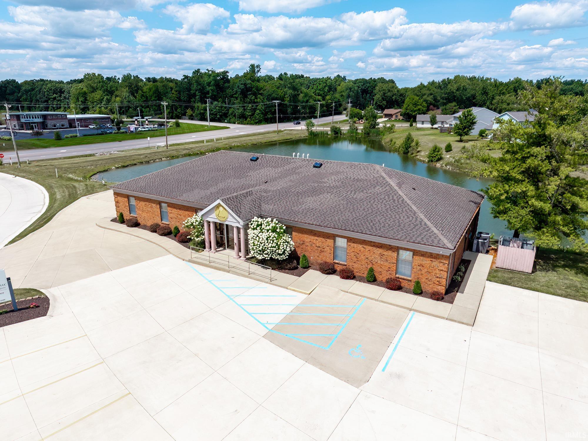 Aerial view of a brick commercial building beside a pond, with a large parking lot and accessible spaces.