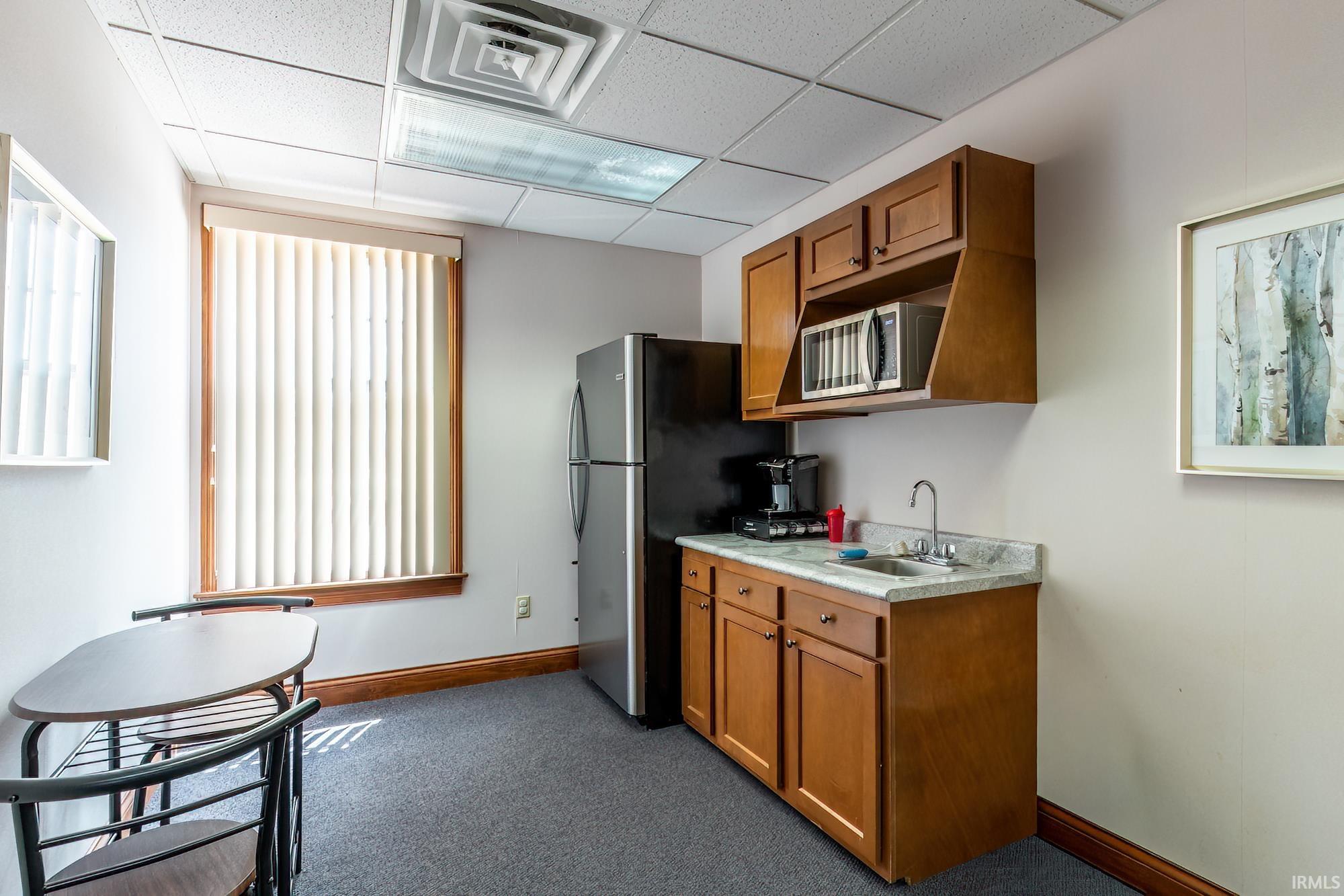 Compact kitchenette with wood cabinets, stainless refrigerator, sink, microwave, and a small table.