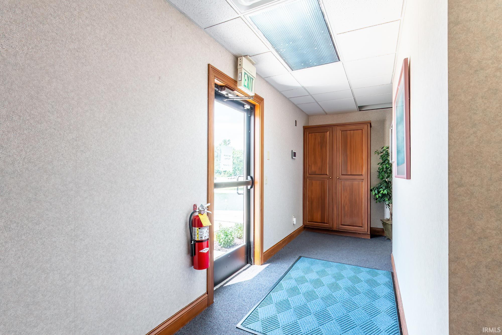 Office entry hallway with a glass exit door, wooden storage cabinet, and blue patterned floor mat.