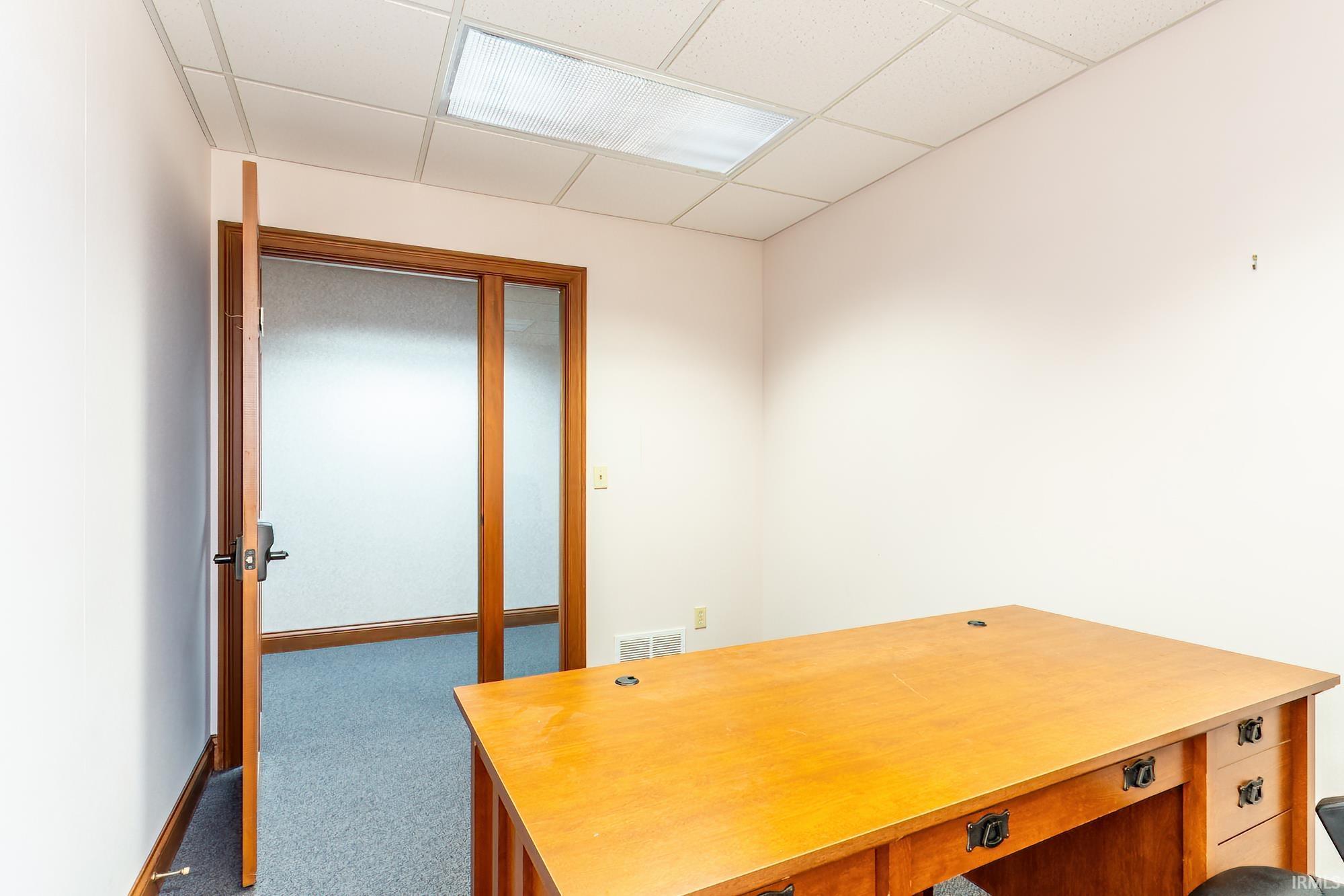 Office with a large wooden desk, blue carpet, and a frosted-glass doorway.