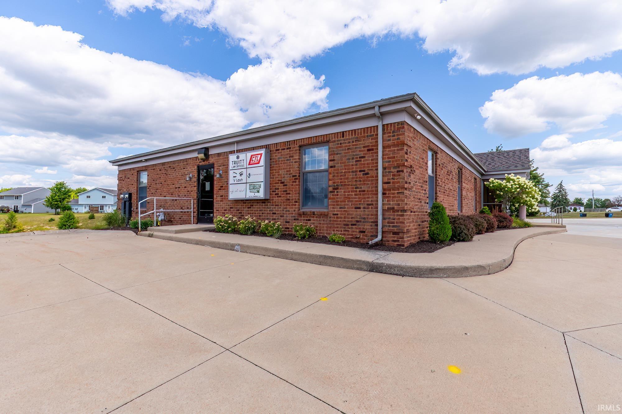 Red brick office building with a tenant directory, accessible entrance ramp, and landscaped frontage.