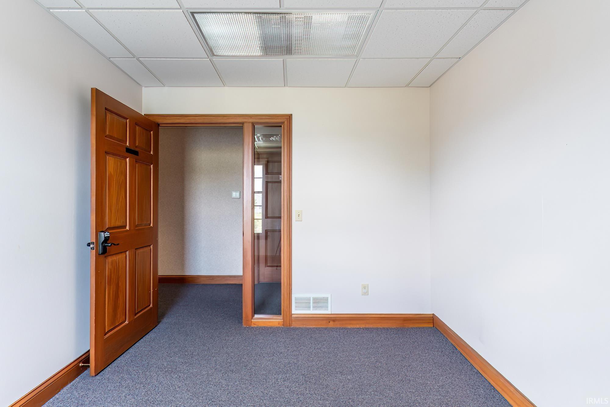 Empty office with blue-gray carpet, wood trim, and an open paneled door.