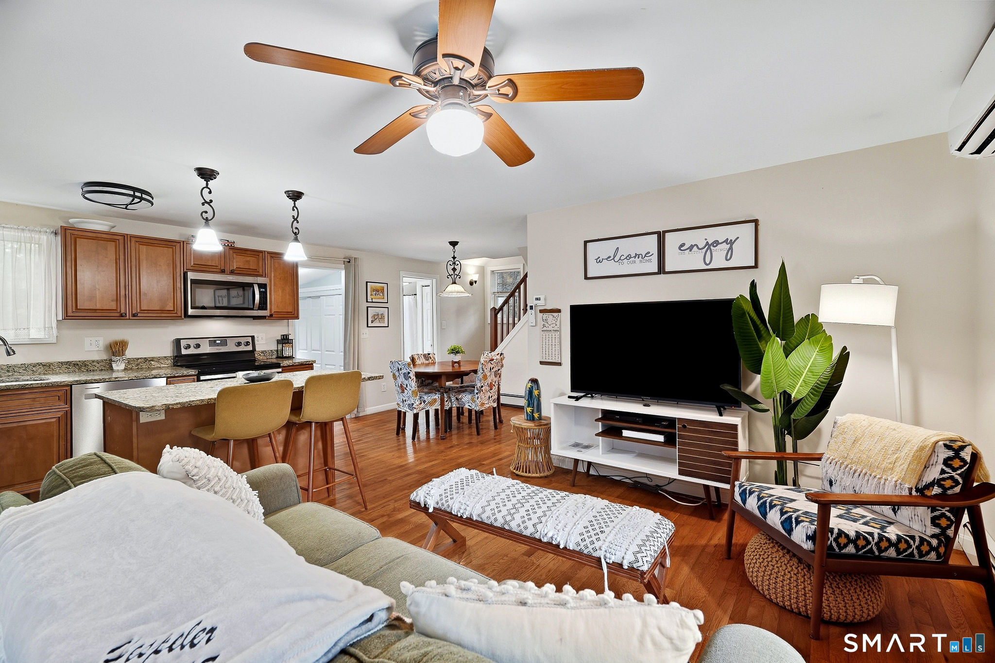 Open-plan living room and kitchen with hardwood floors, wood cabinets, breakfast bar, and furnished seating area.