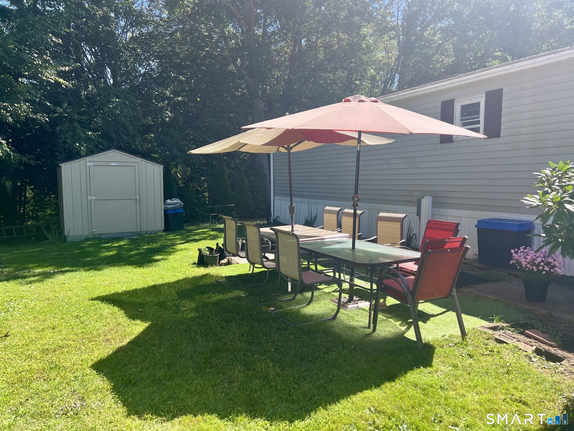Backyard patio with a shaded dining set beside the house, lawn, and storage shed.