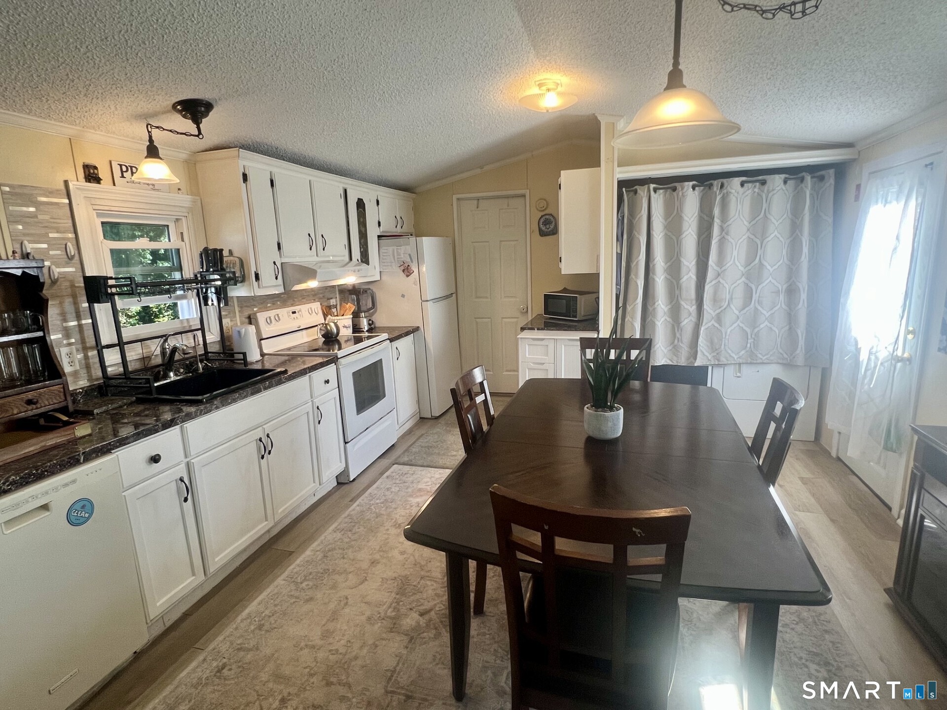Kitchen and dining area with white cabinets, dark countertops, and a large wood table.