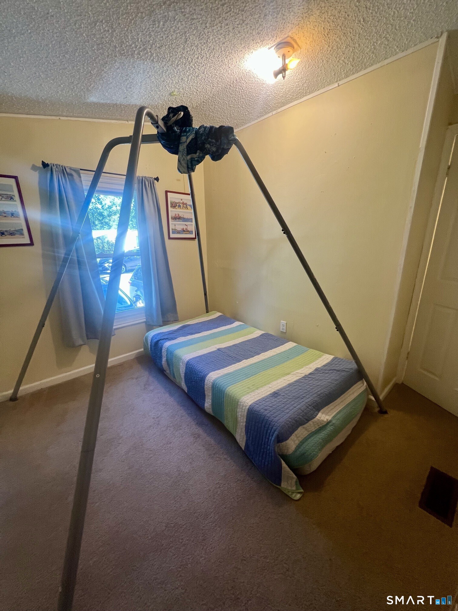 Small bedroom with a striped single bed beneath a large metal frame.