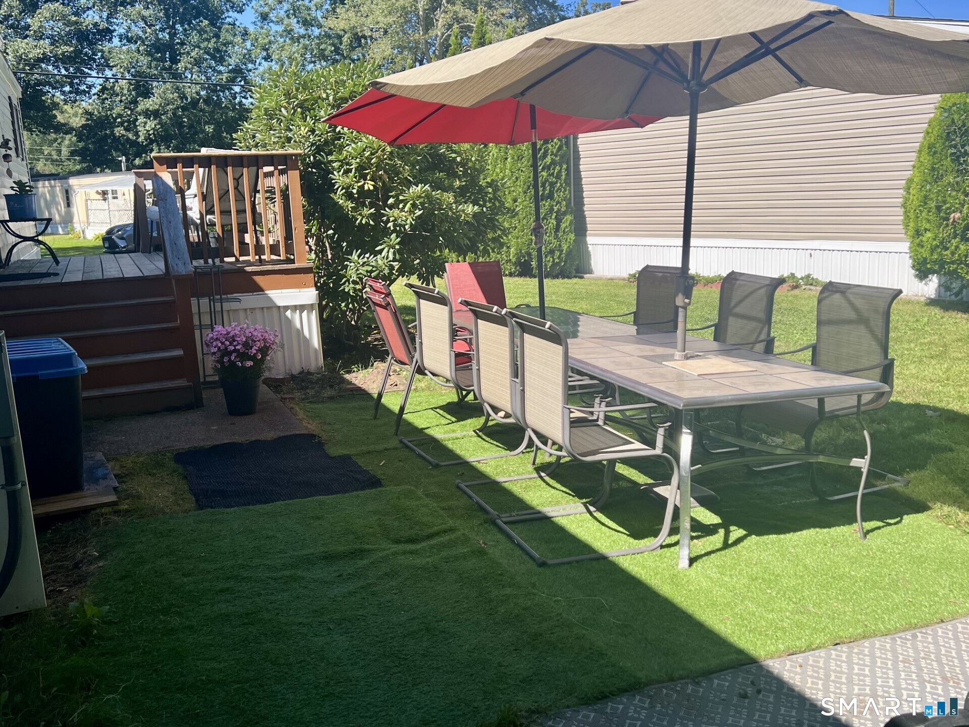 Backyard patio with a dining table beneath a large umbrella beside a raised wooden deck.