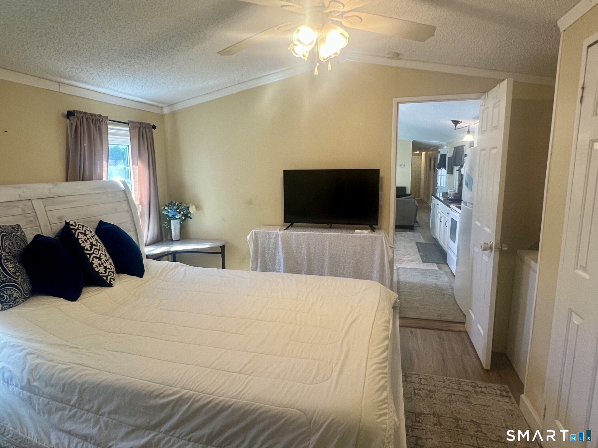 Bedroom with a large white bed, dark pillows, and a doorway opening toward the kitchen.