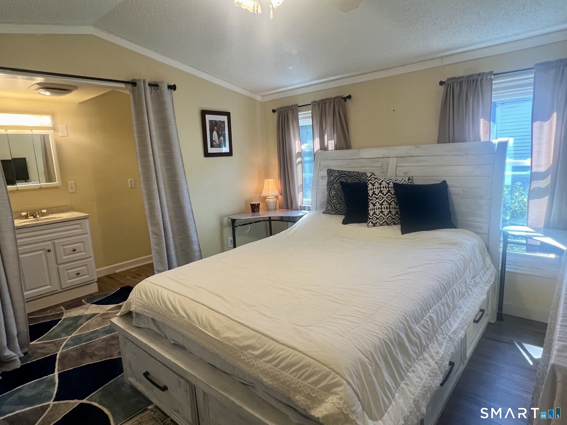 Bedroom with a large white bed, dark patterned pillows, and a vanity area.