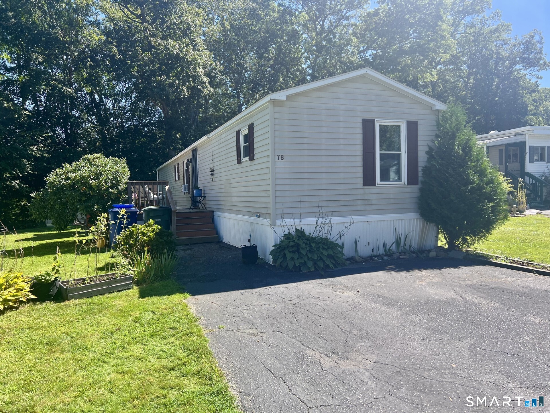 Light-sided home with dark shutters, entry steps, landscaped lawn, and paved driveway.