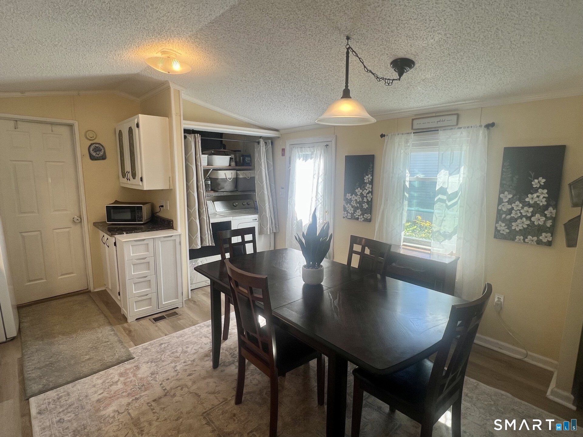 Dining area with a dark table beside a compact kitchen and curtained laundry nook.