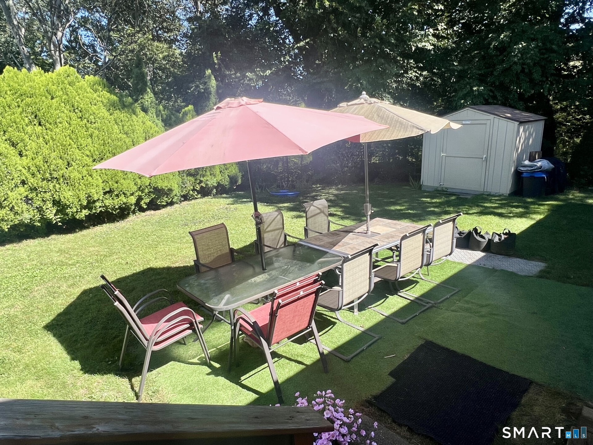 Backyard patio with outdoor dining tables, chairs, and colorful umbrellas on a sunny lawn.