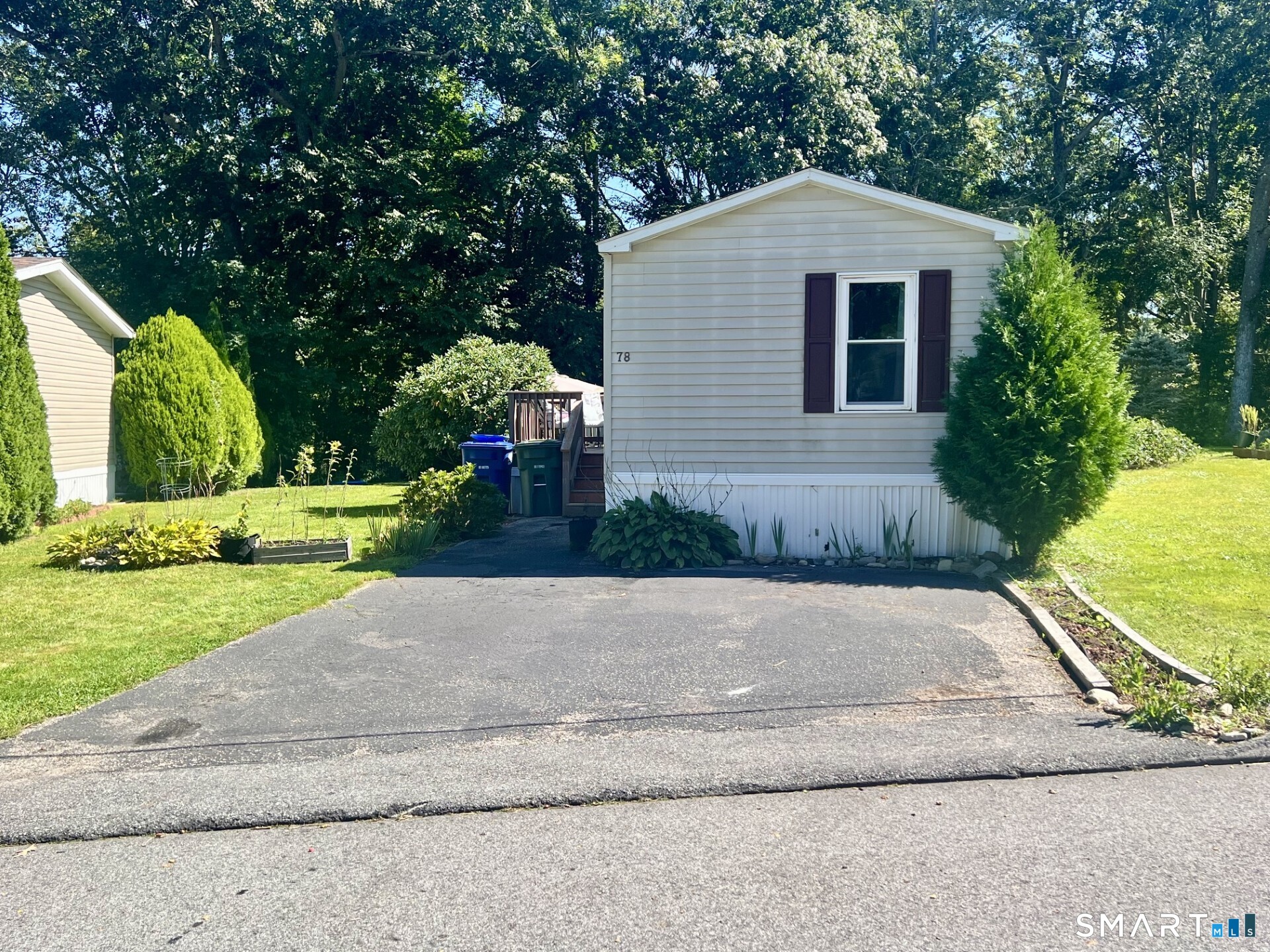 Light-colored home with dark window shutters, a paved driveway, and landscaped lawn beneath mature trees.
