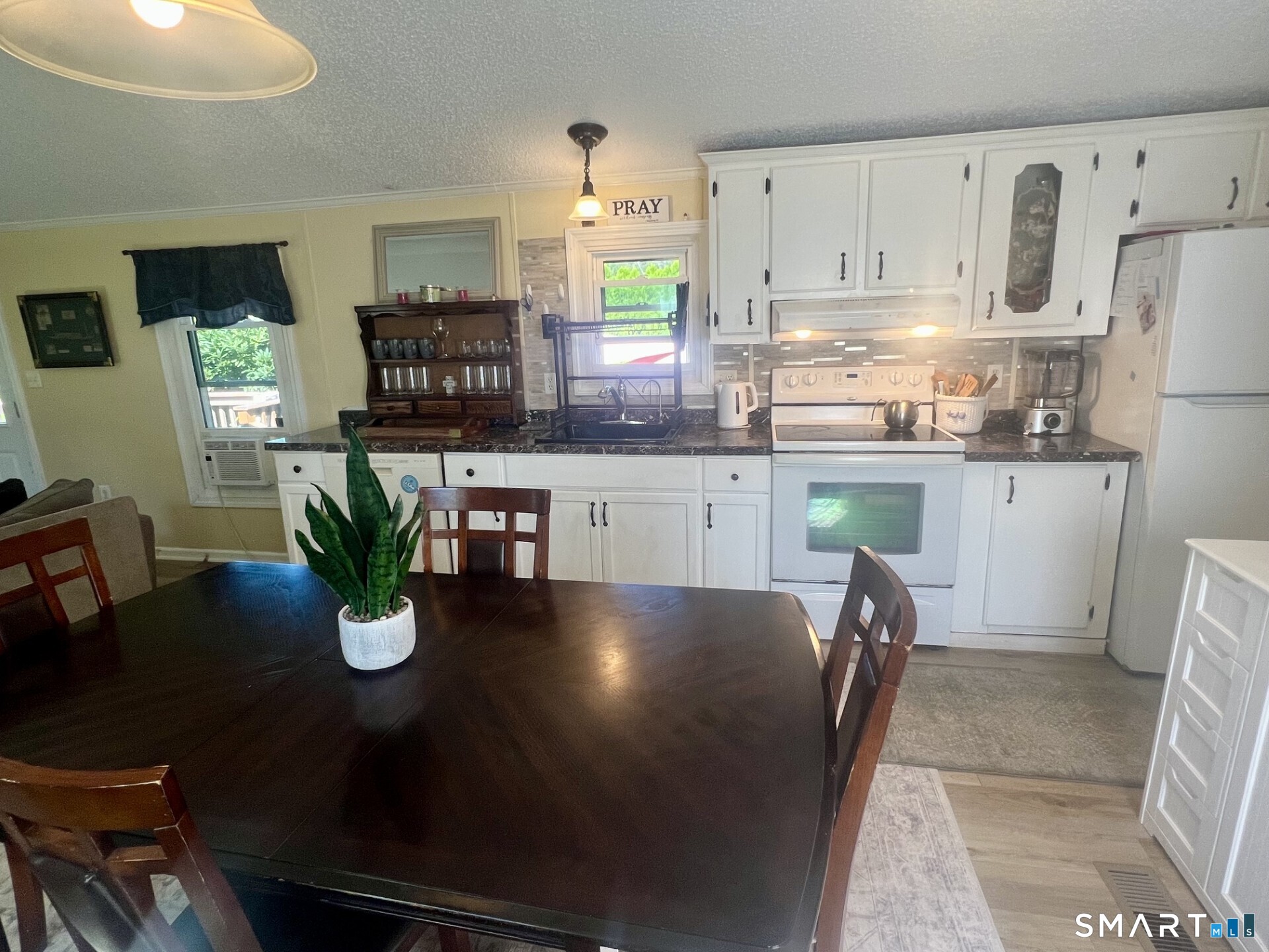Kitchen with white cabinets, dark countertops, and a dining table with a potted plant.