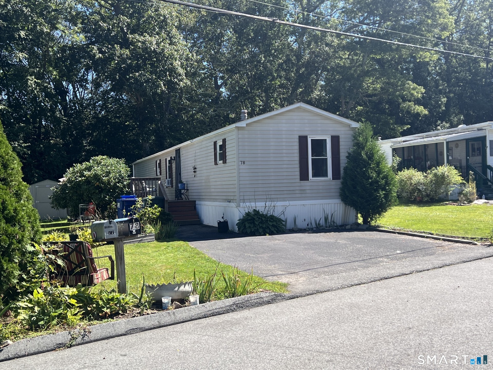 Single-story home with dark shutters, a small porch, paved driveway, and mature trees.