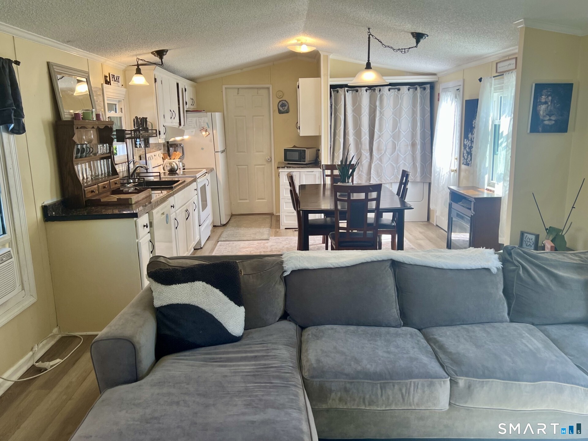 Open-plan kitchen and dining area viewed over a gray sectional sofa, with white cabinets and a dark dining table.