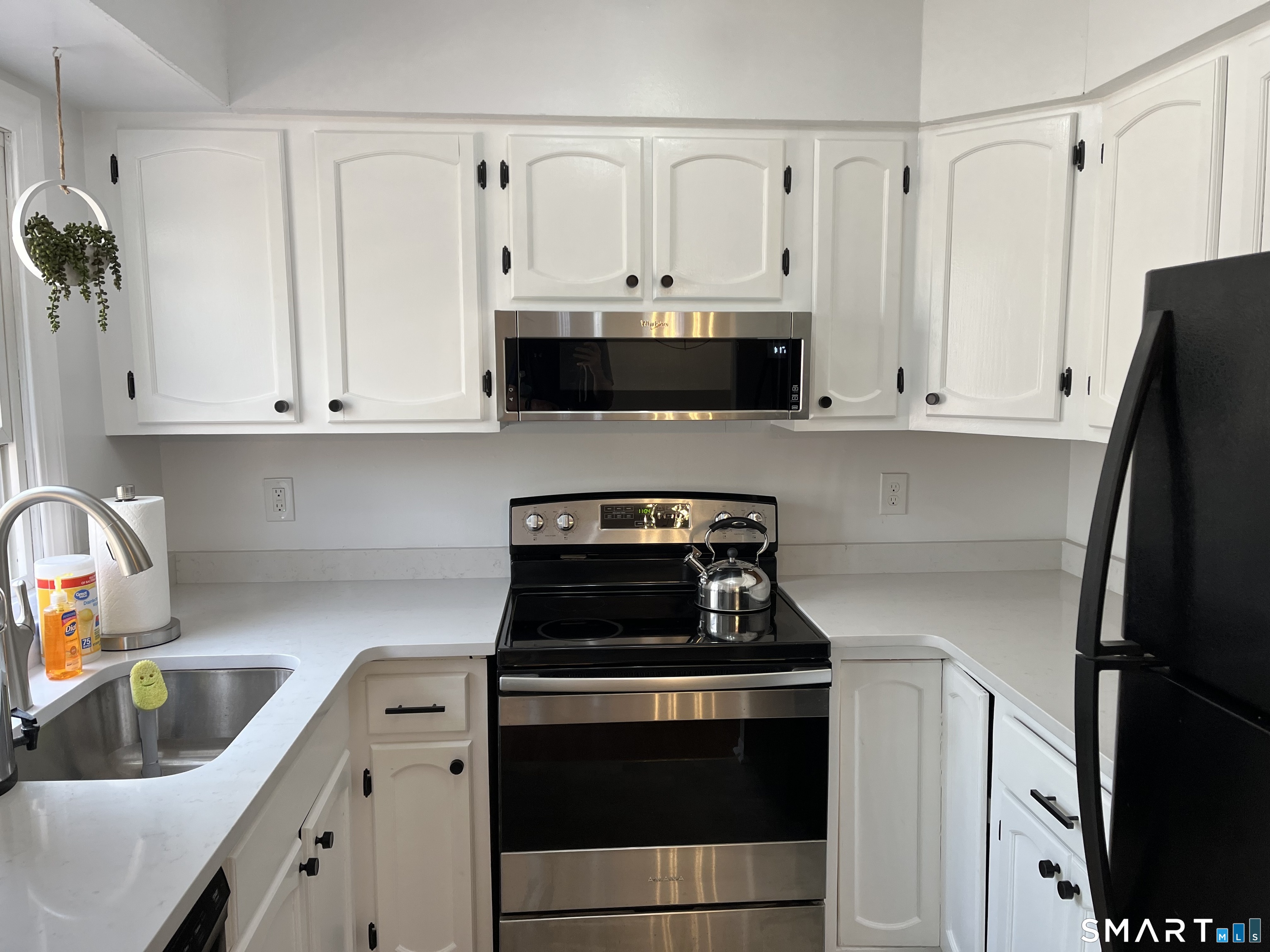 Kitchen with white cabinets, stainless-steel range and microwave, and a kettle on the stovetop.