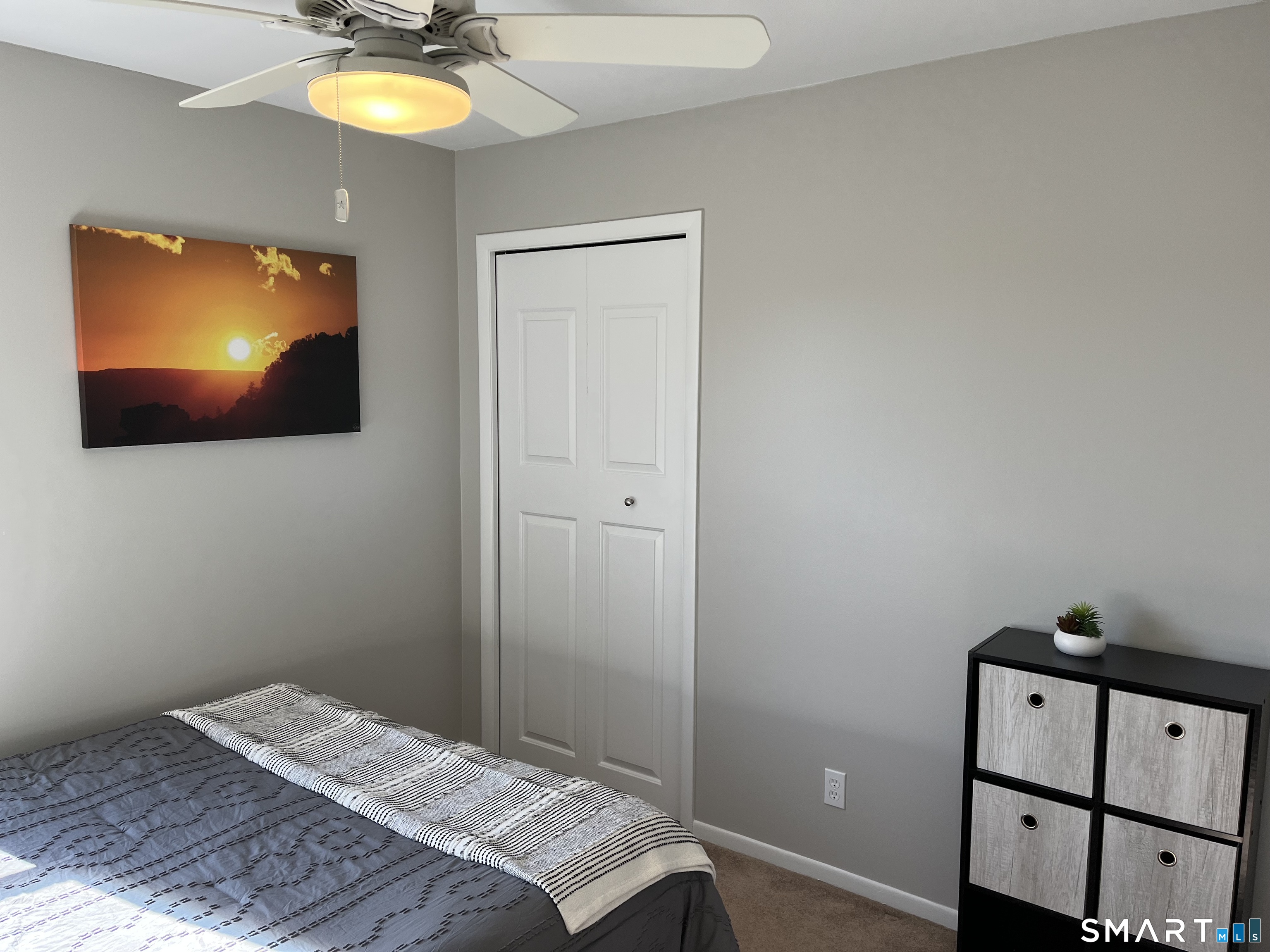 Bedroom with a gray bedspread, white closet doors, ceiling fan, and black cube storage unit.