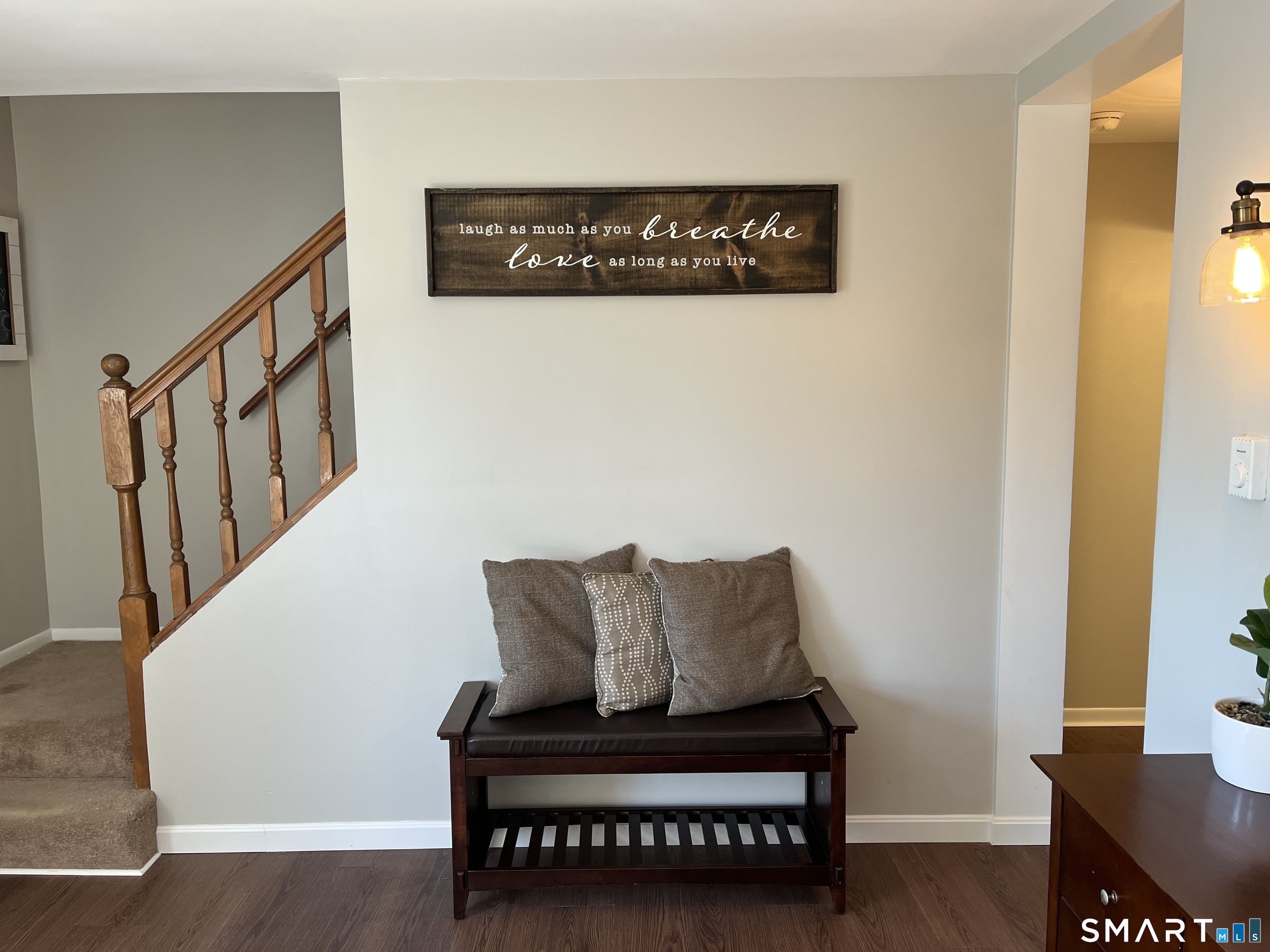 Furnished entryway with a wooden staircase, a bench with pillows, and a rustic wall sign.
