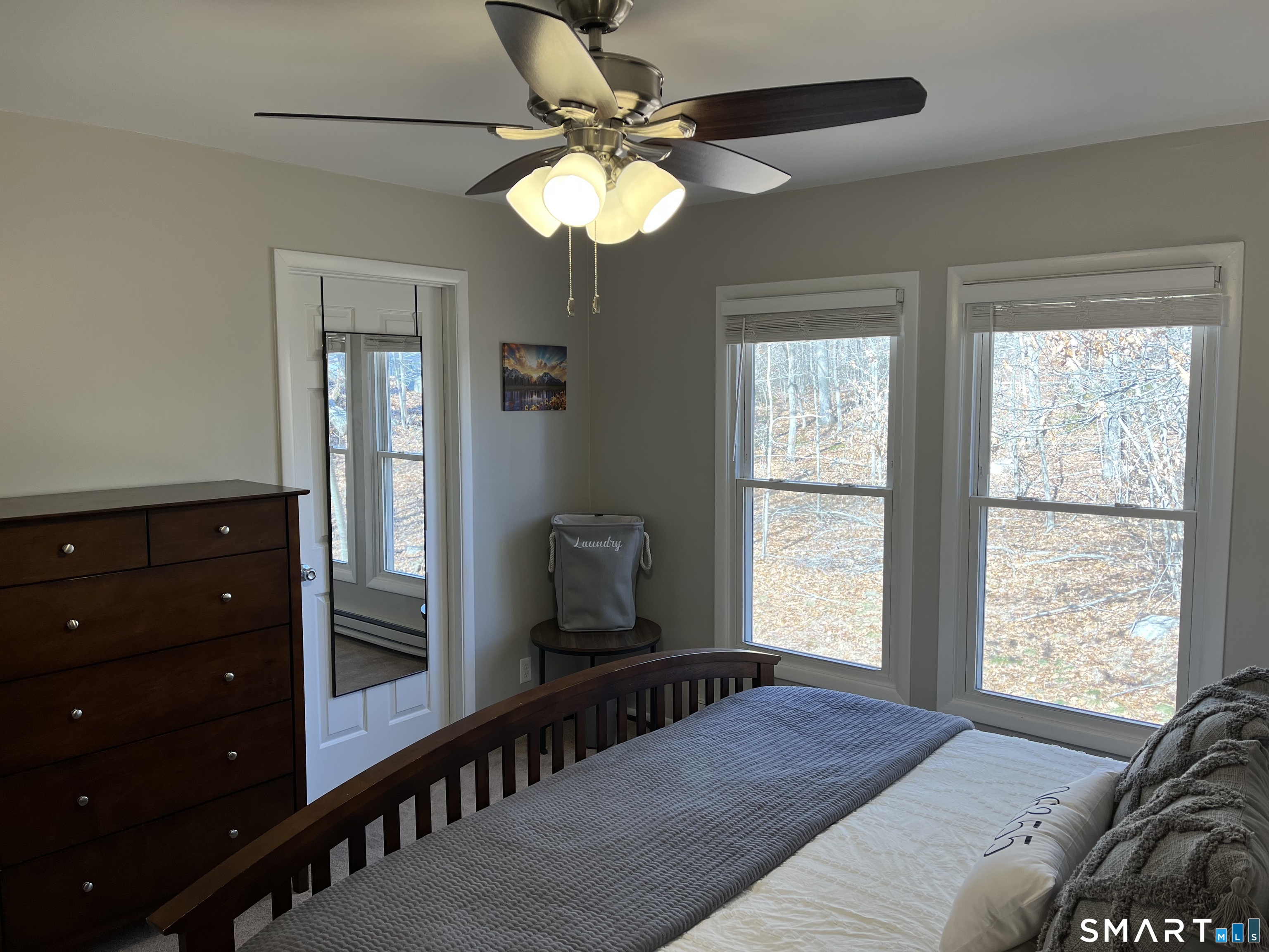 Furnished bedroom with a dark wooden bed and large windows overlooking autumn woodland.