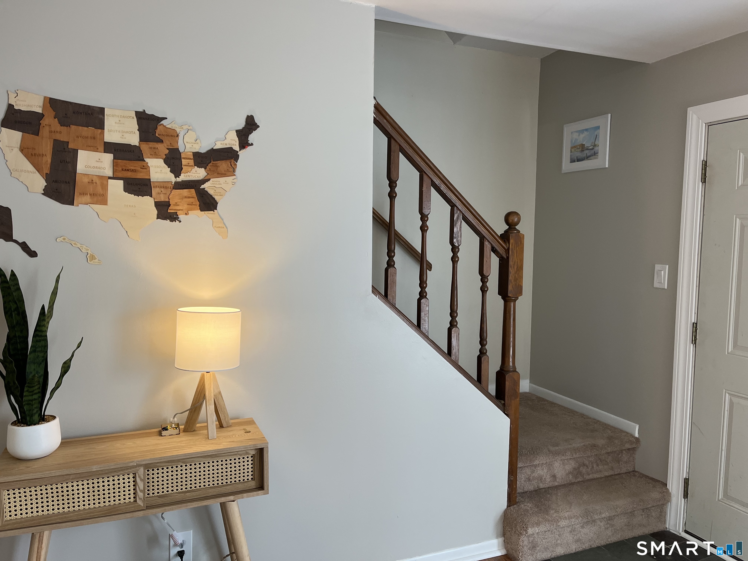 Entryway with carpeted stairs, dark wood railing, console table, glowing lamp, and wooden U.S. map.