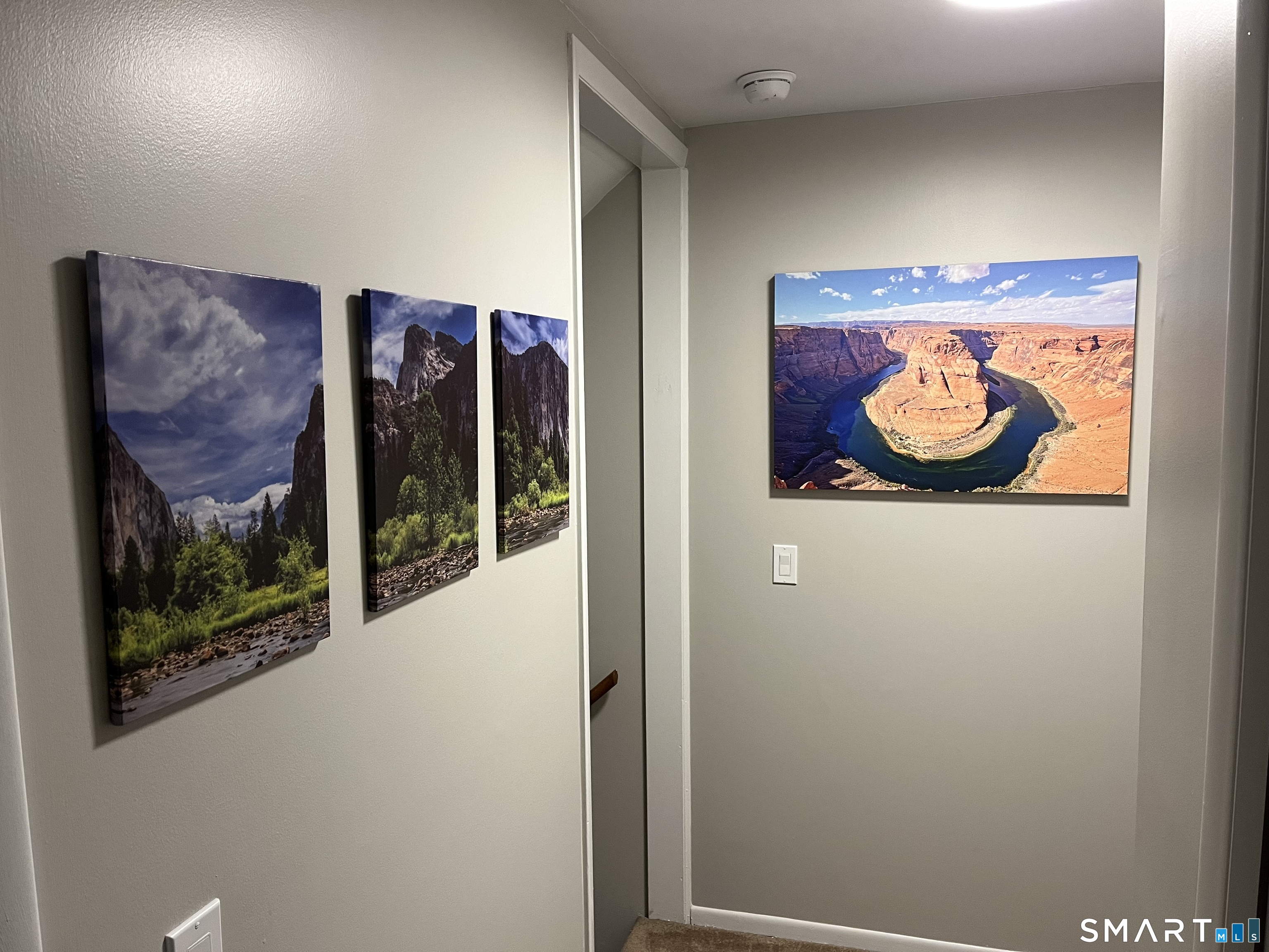 Narrow hallway with neutral walls and framed landscape photographs, including a red-rock canyon river scene.