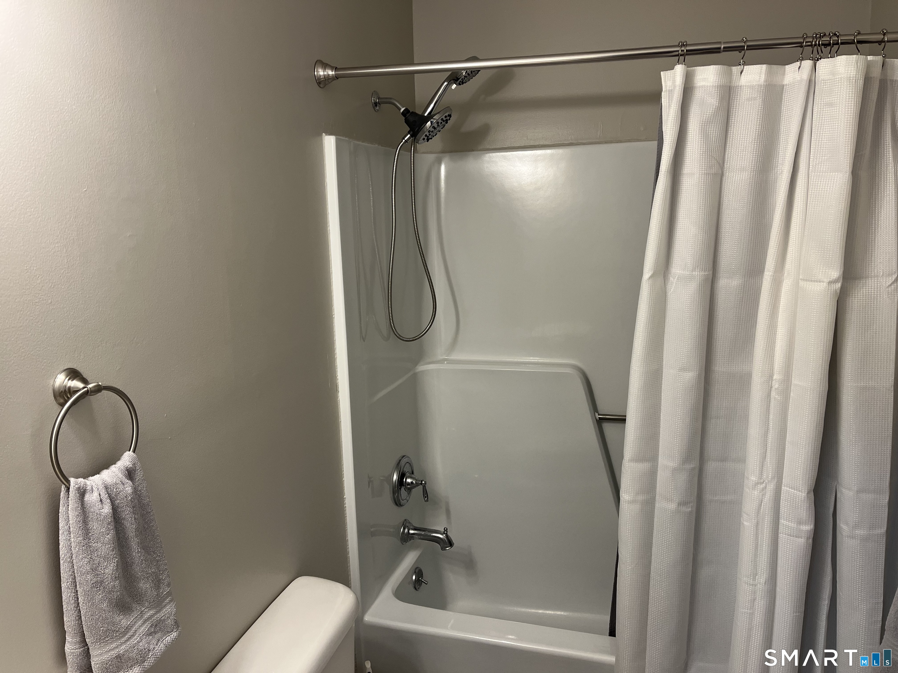 Bathroom tub and shower with chrome fixtures, handheld showerhead, and white curtain.