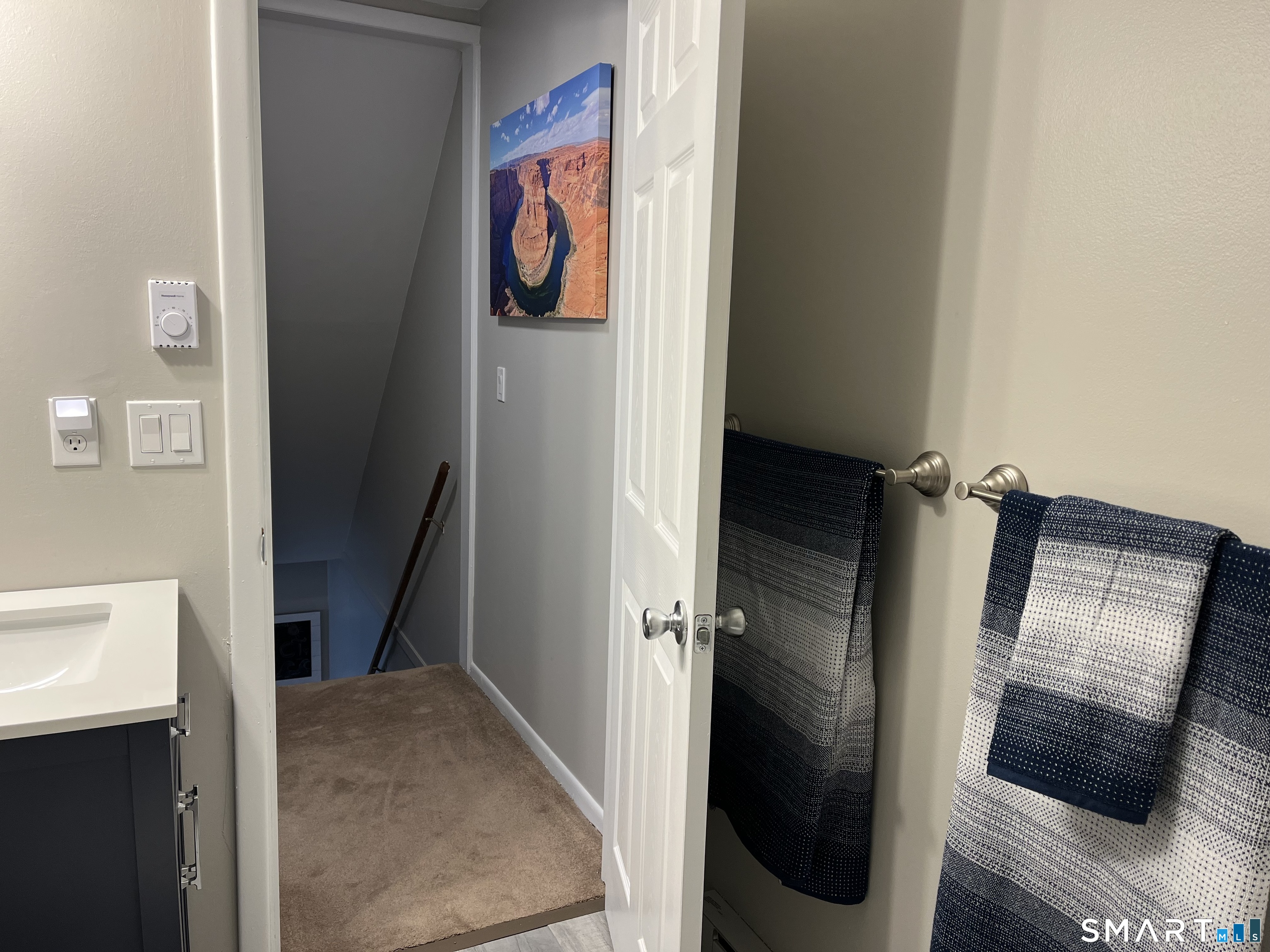 Bathroom vanity and patterned towels beside an open doorway to a carpeted stair landing.