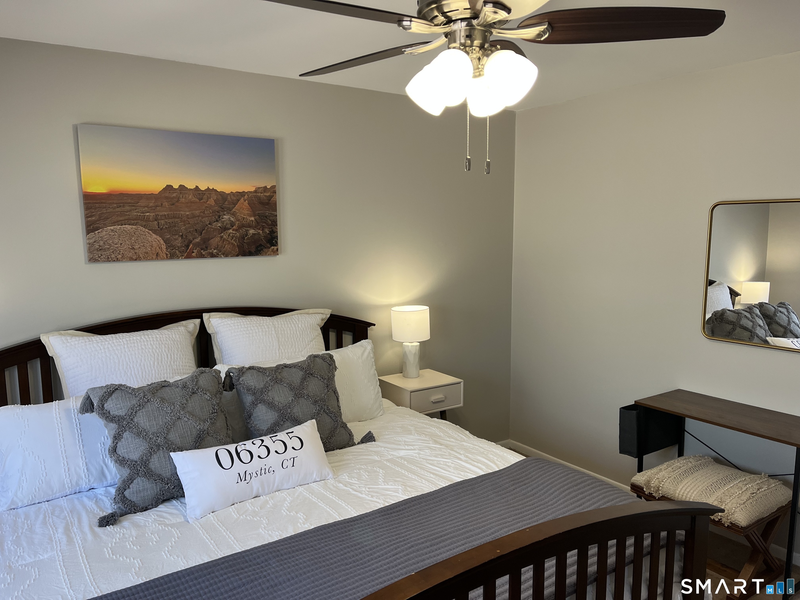 Furnished bedroom with white bedding, gray pillows, and a Mystic, CT accent pillow.
