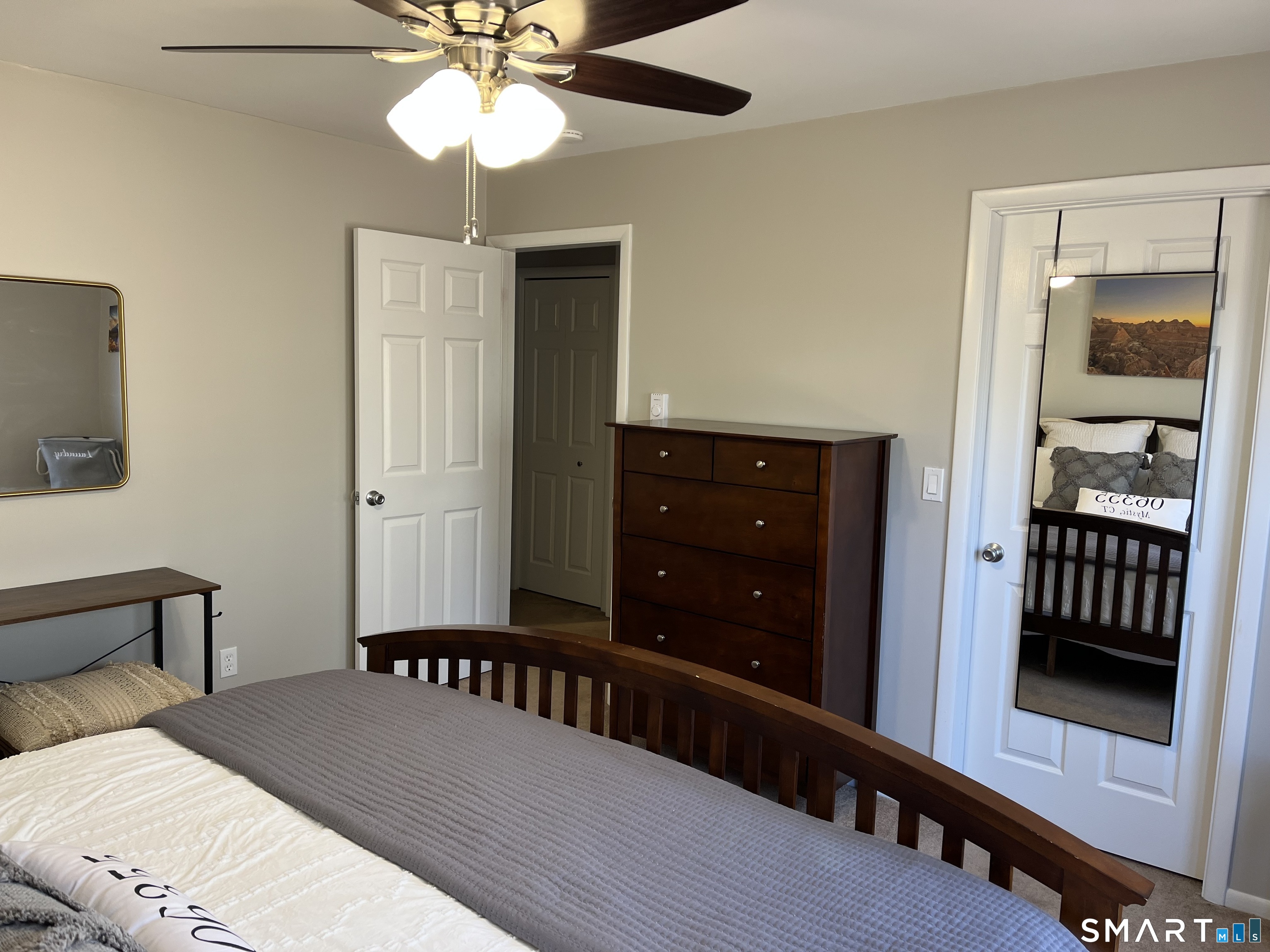 Furnished bedroom with gray bedding, a dark wood bed and dresser, and a mirrored door reflecting a crib.