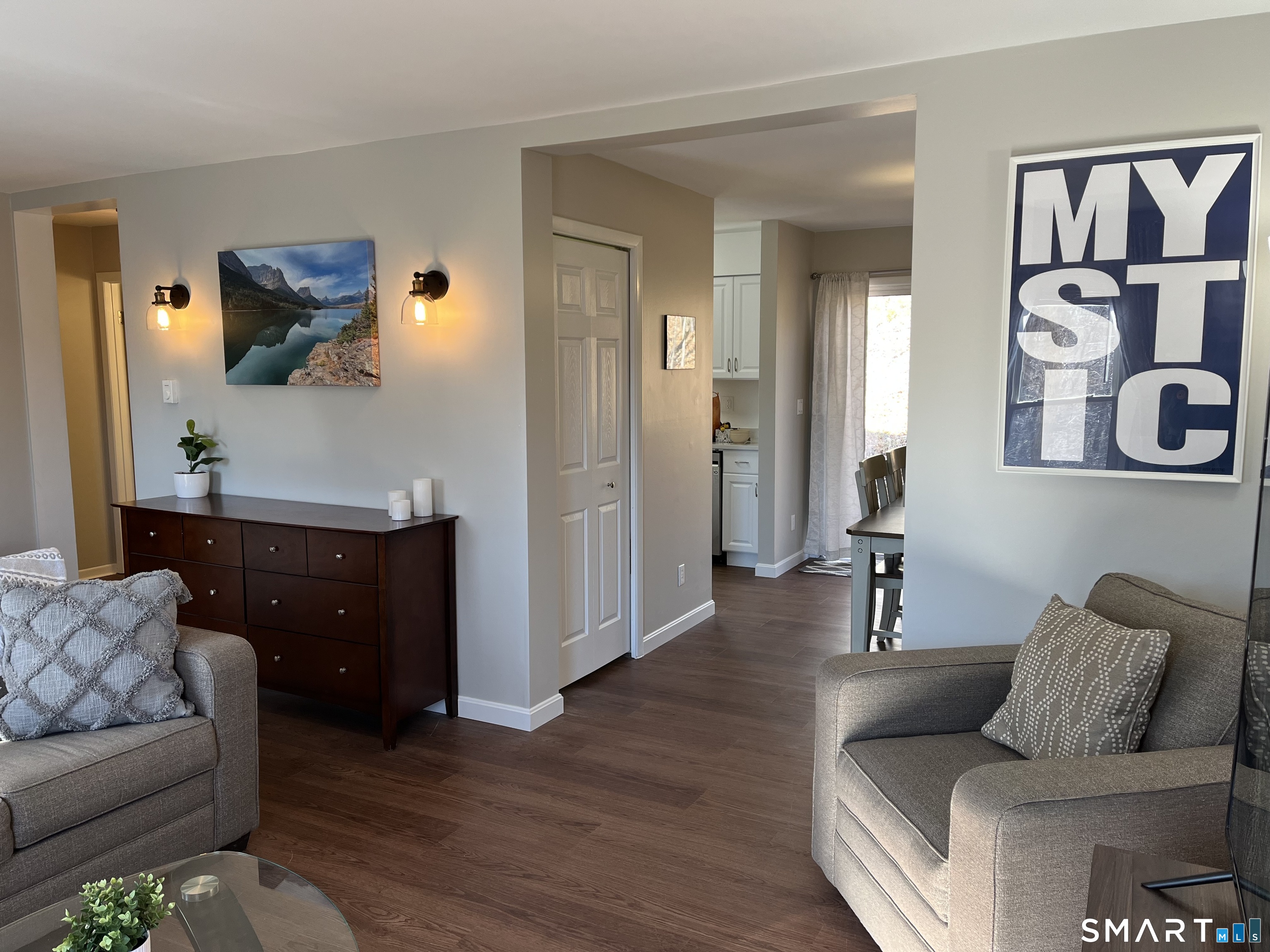 Furnished living room with gray armchairs, dark wood flooring, and a large framed MYSTIC print.