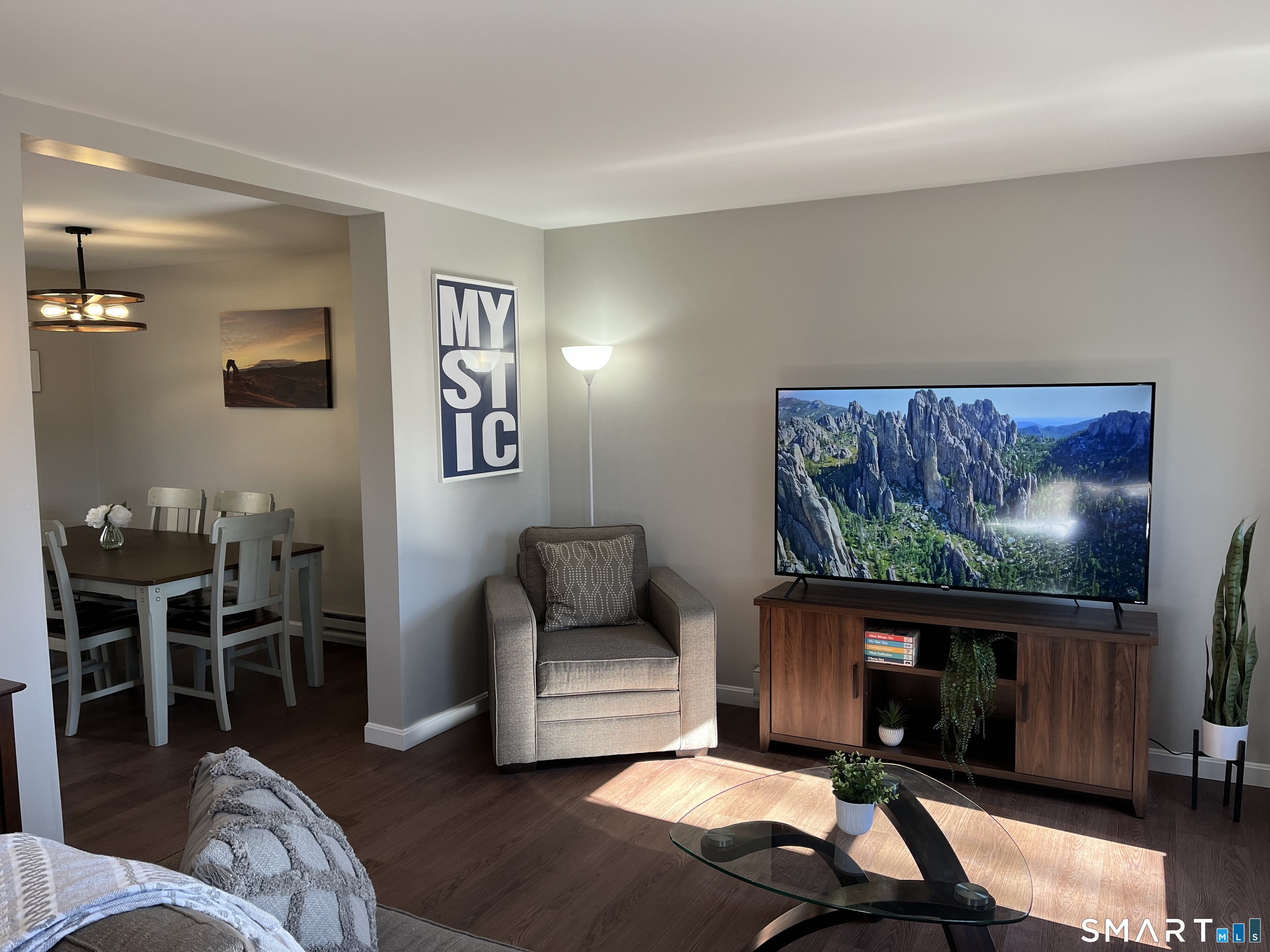 Living room with a television, gray armchair, glass coffee table, and adjoining dining area.