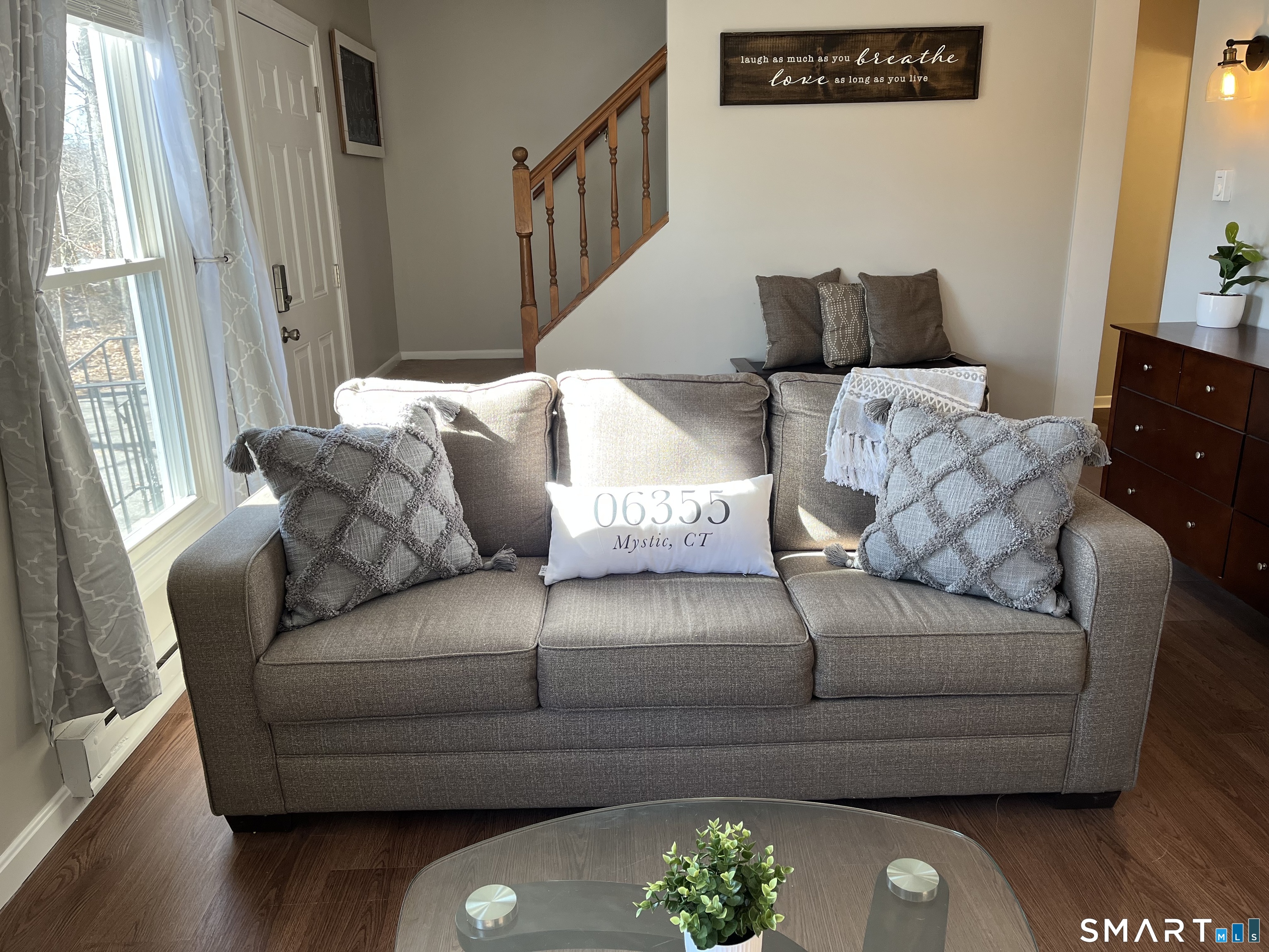 Furnished living room with a gray sofa, glass coffee table, and wooden staircase.