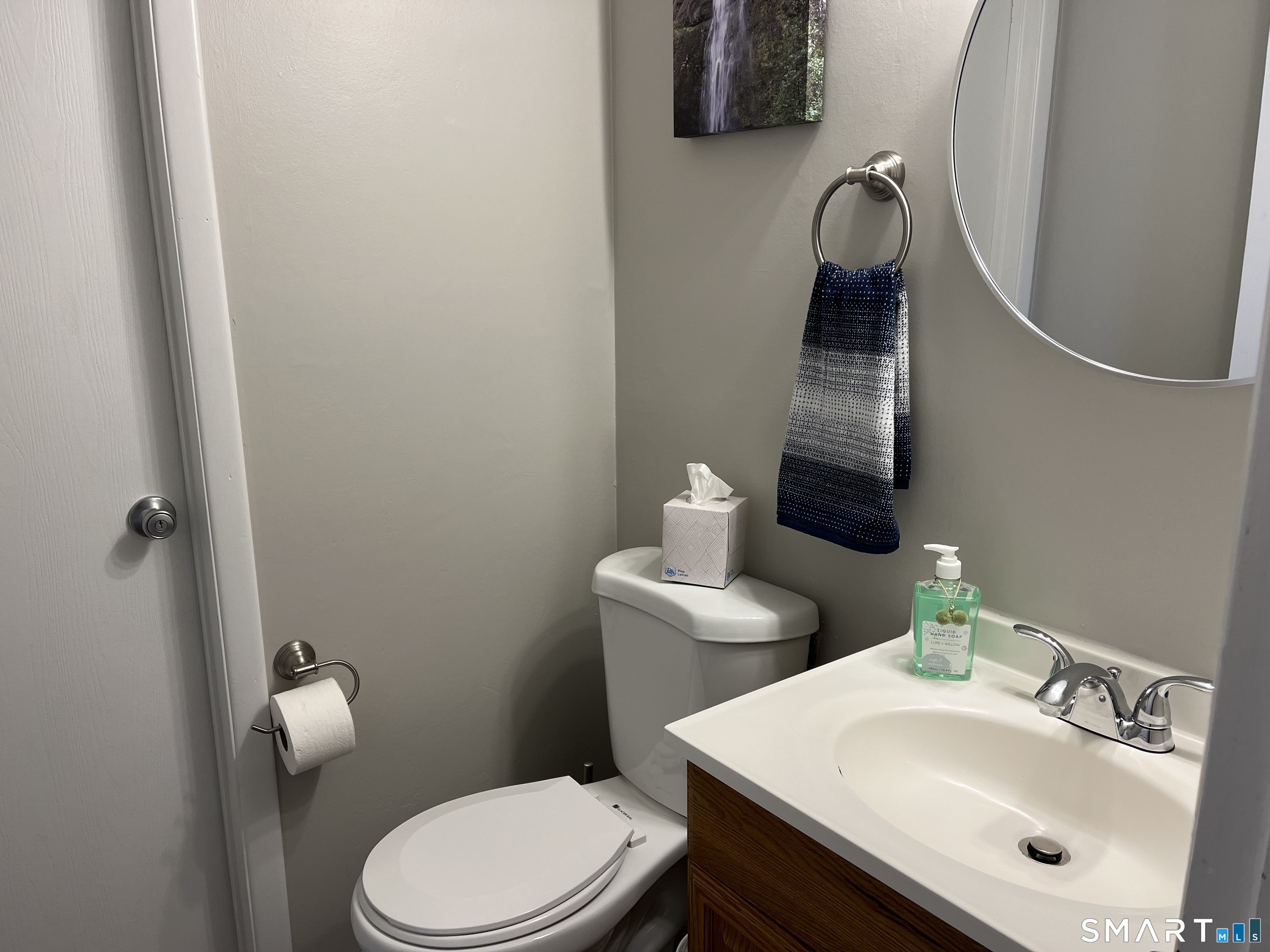 Bathroom with a white toilet, wood vanity, round mirror, and navy-and-white hand towel.