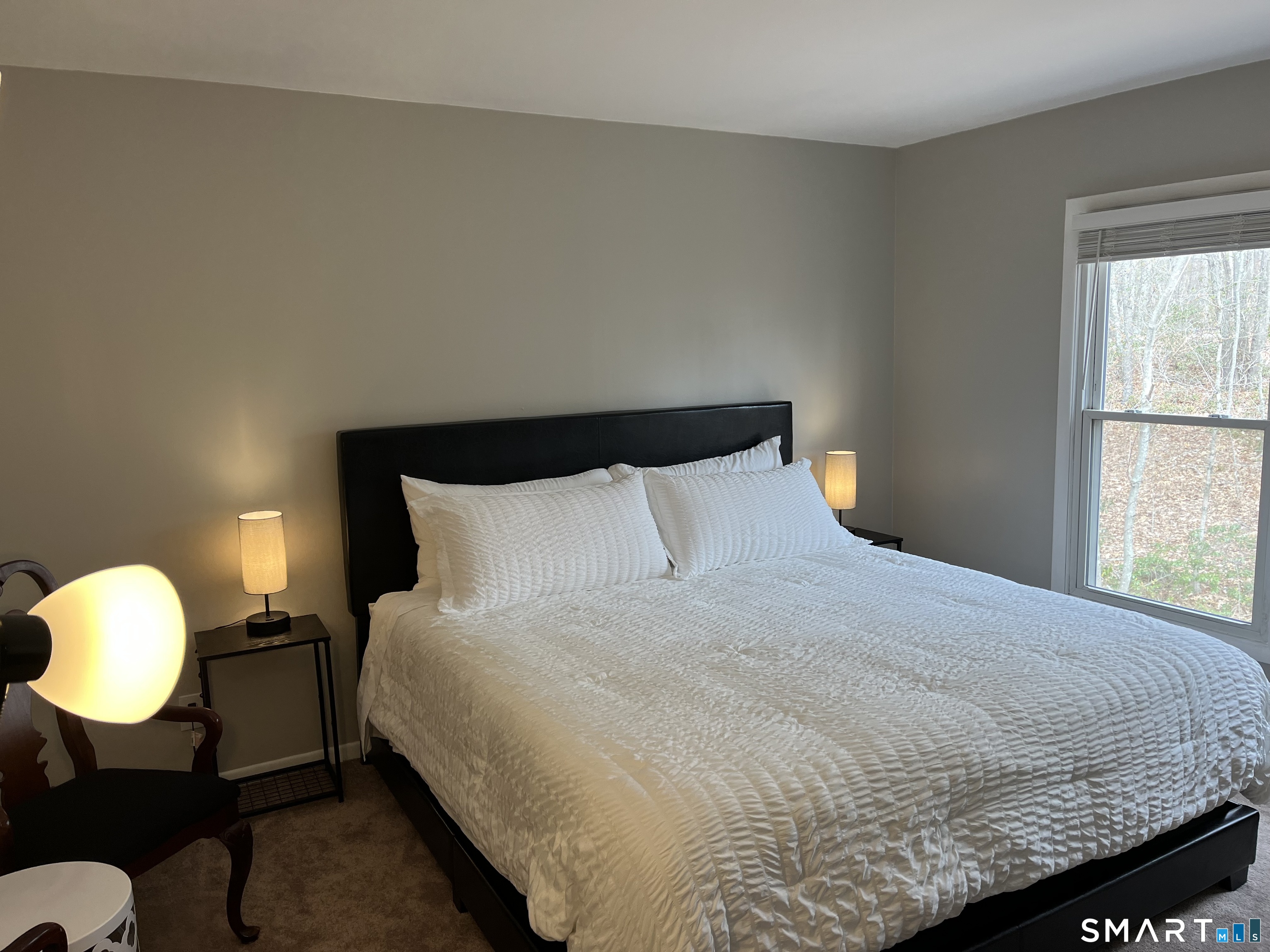 Bedroom with a large bed, white textured bedding, black headboard, and a window overlooking trees.