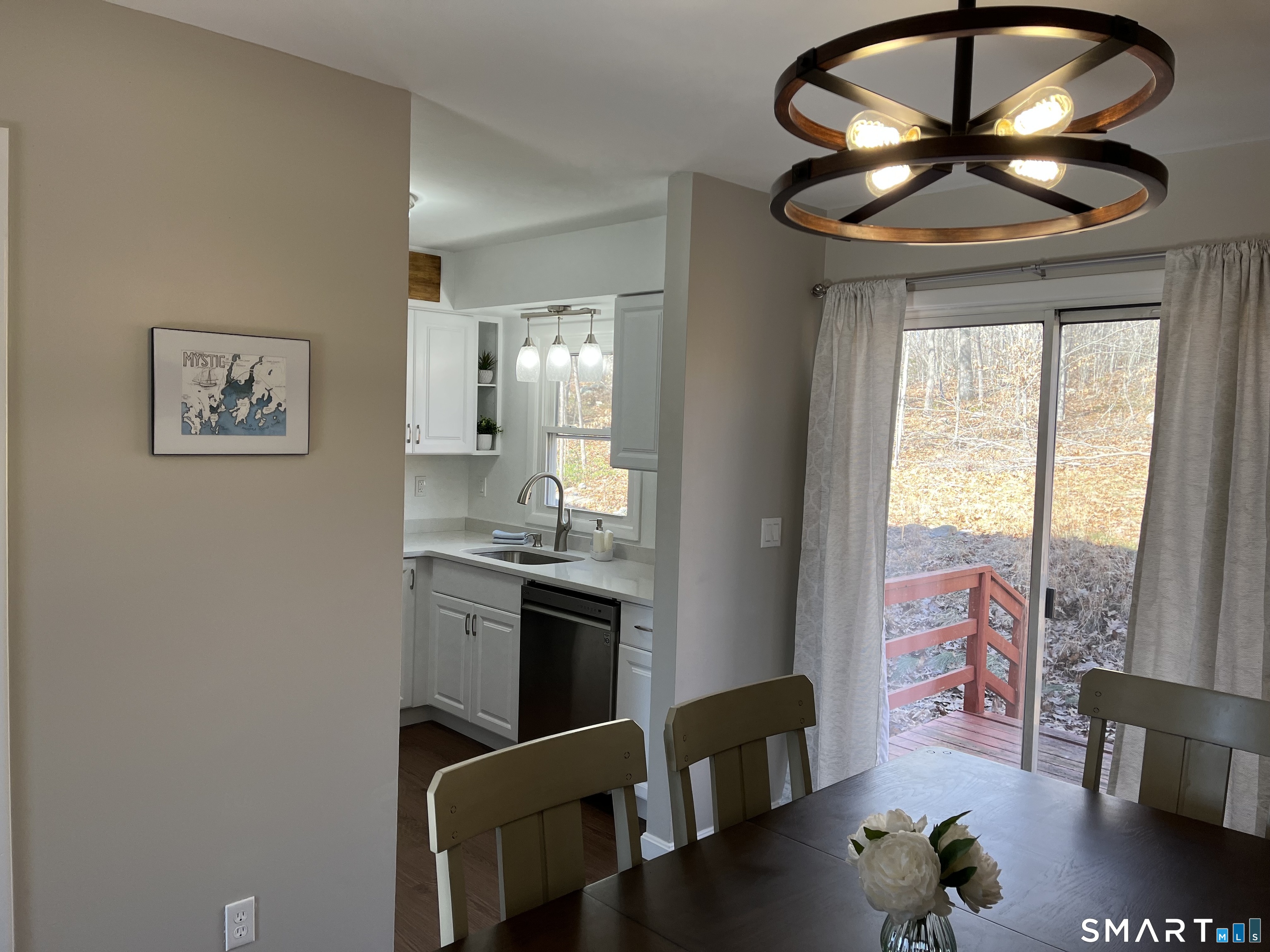 Dining area with a modern circular pendant, adjoining white kitchen, and sliding doors to a wooded deck.