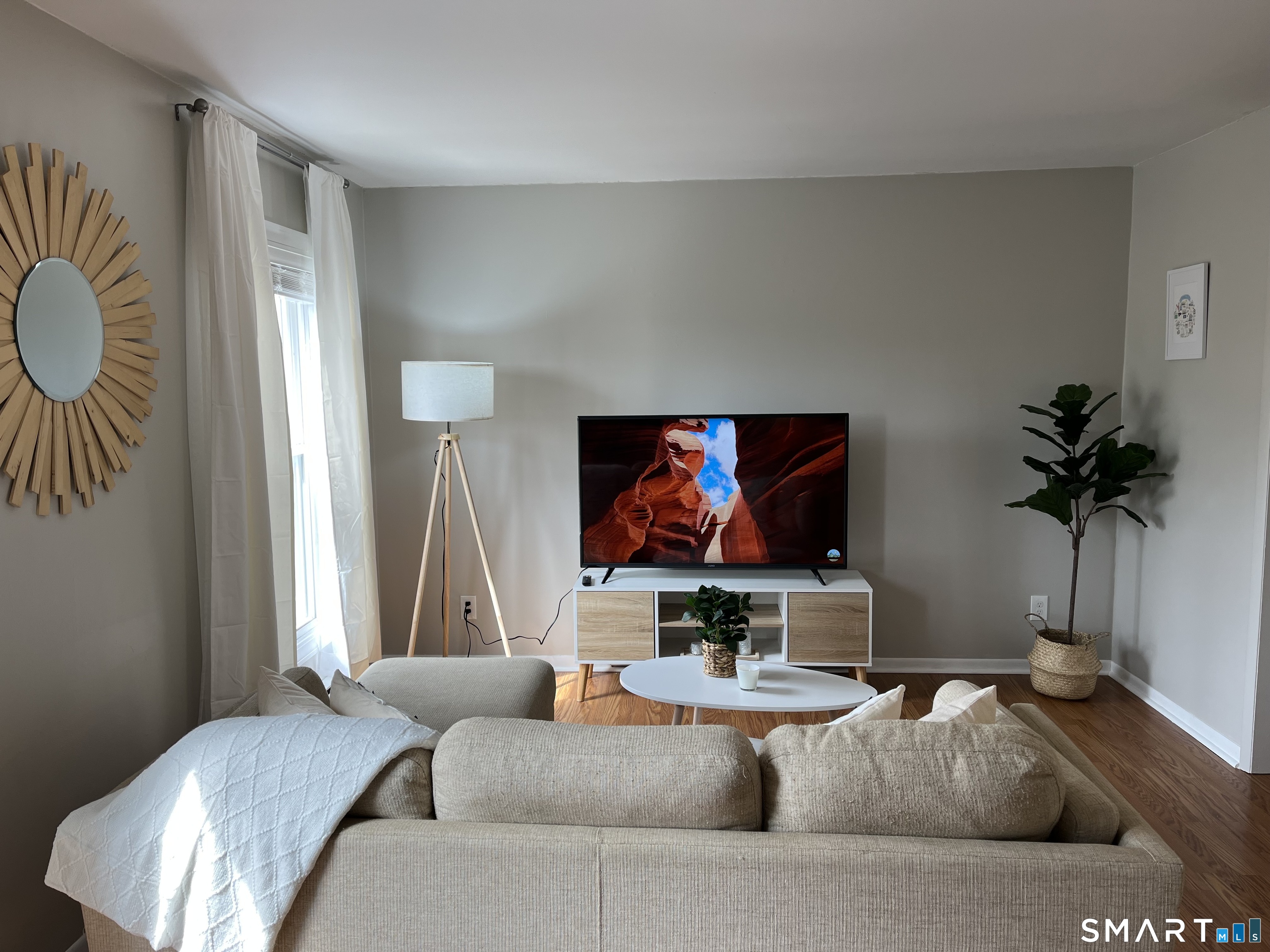 Furnished living room with hardwood floors, a beige sofa, and a television console.