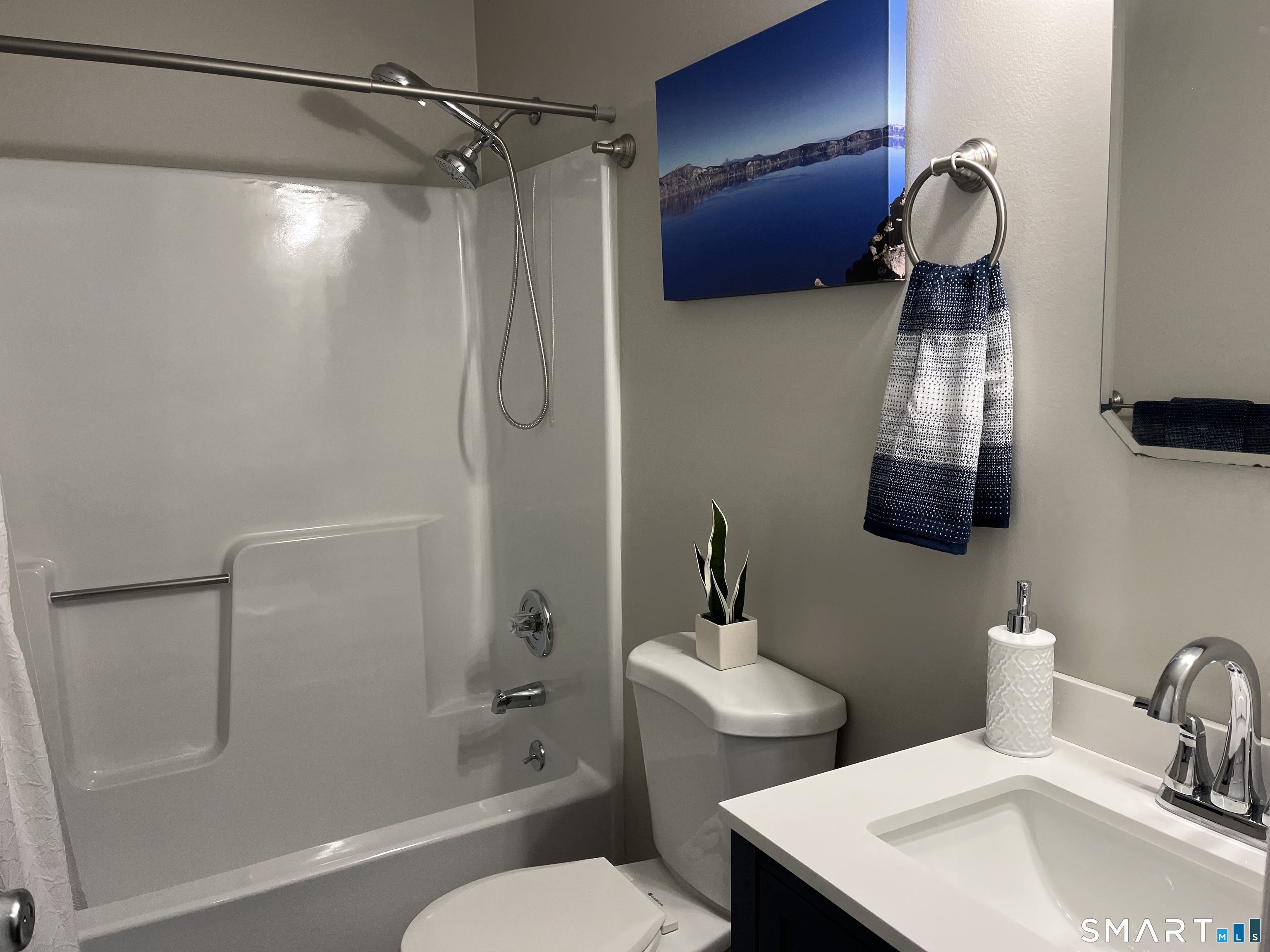 Bathroom with a white tub and shower, toilet, and dark vanity topped by a white sink.
