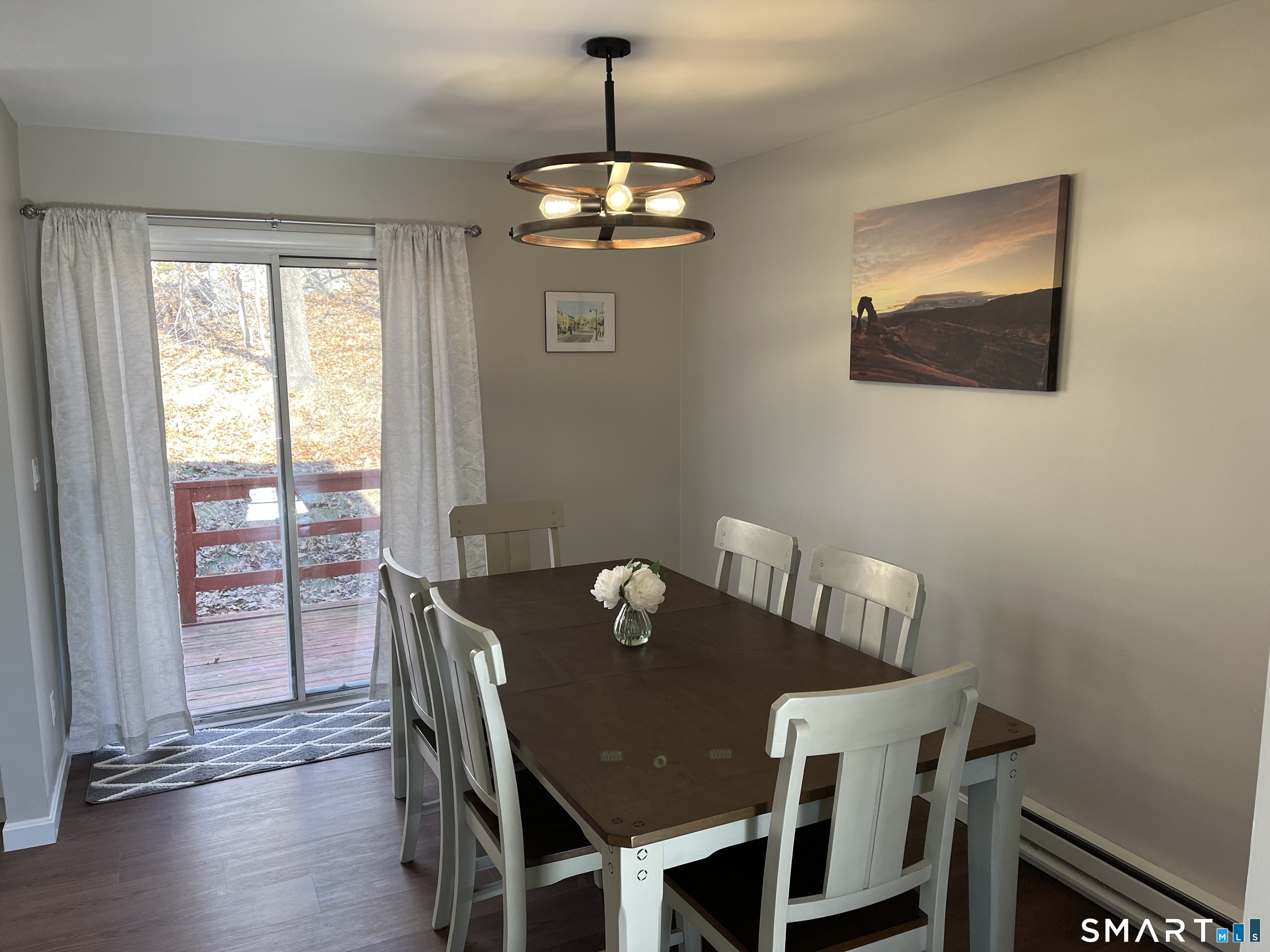 Dining room with a dark wood table, white chairs, and sliding glass door to a deck.